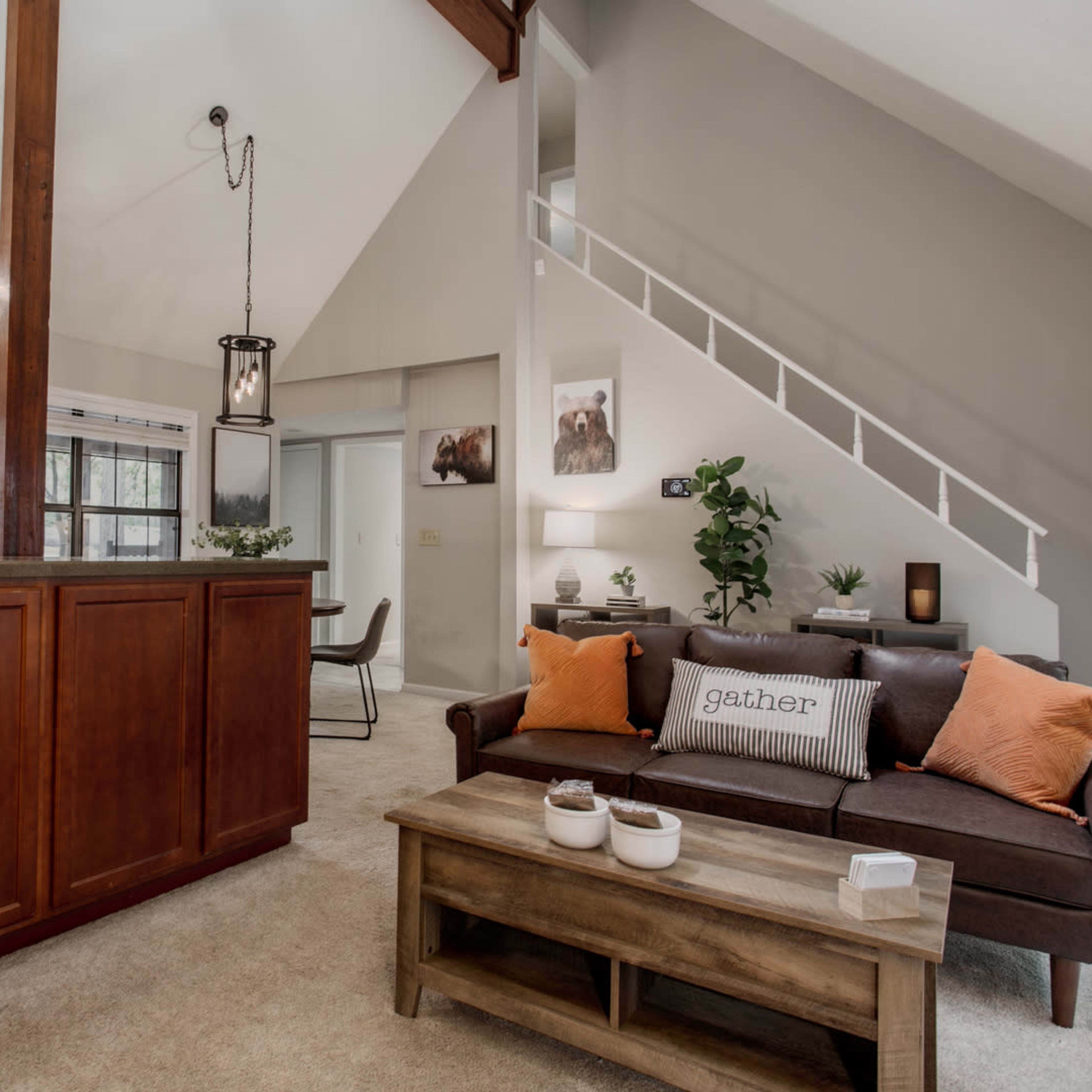 A modern living space featuring a kitchen with wooden cabinets, a brown sofa adorned with cushions, and a dining area visible in the background.