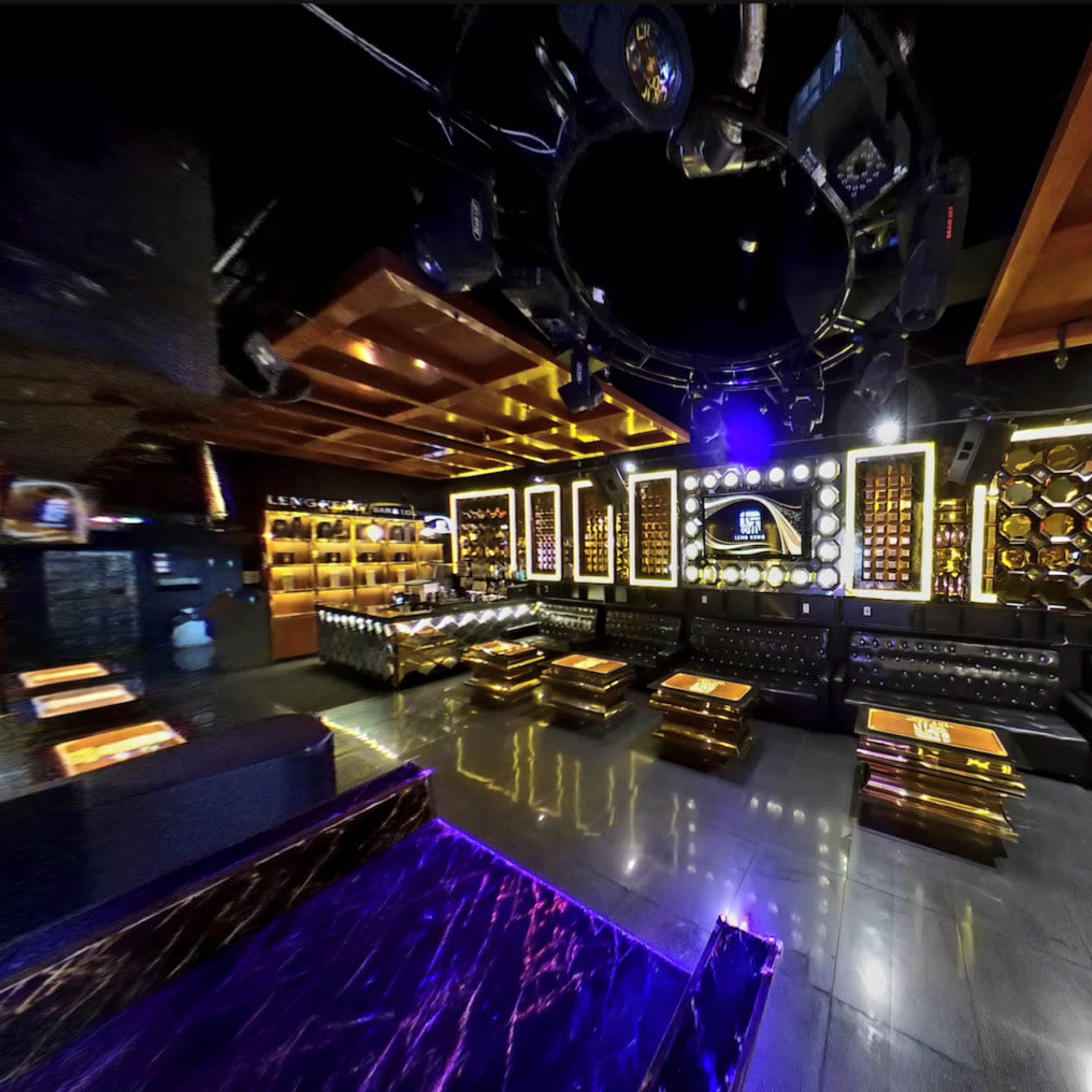 An upscale lounge with leather seating, illuminated decor, and a bar area featuring shelves of bottles.