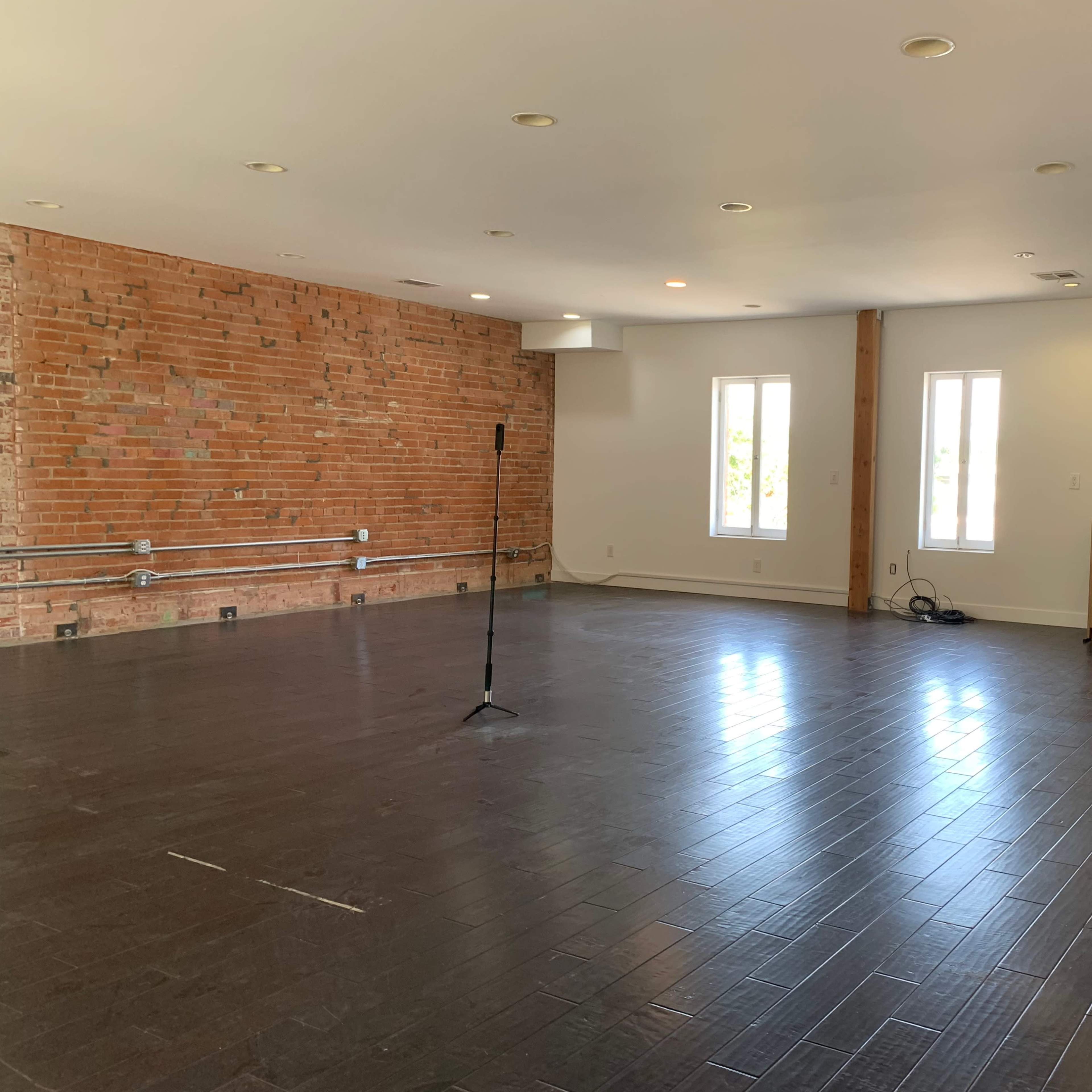 A spacious, open room with a brick accent wall, a microphone stand, and multiple windows allowing natural light.