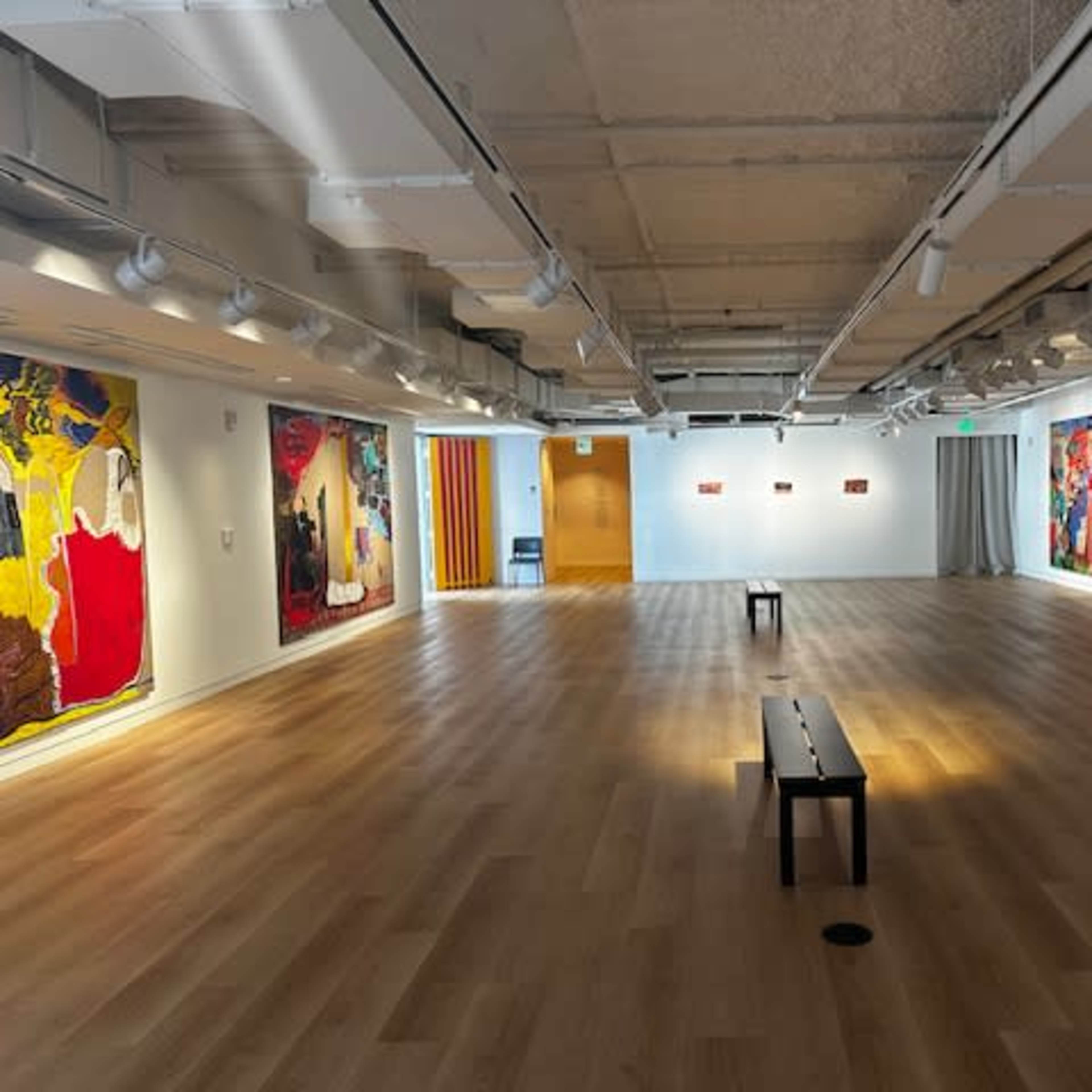 An art gallery featuring large, colorful paintings on the walls and a wooden bench positioned in the center of the room.