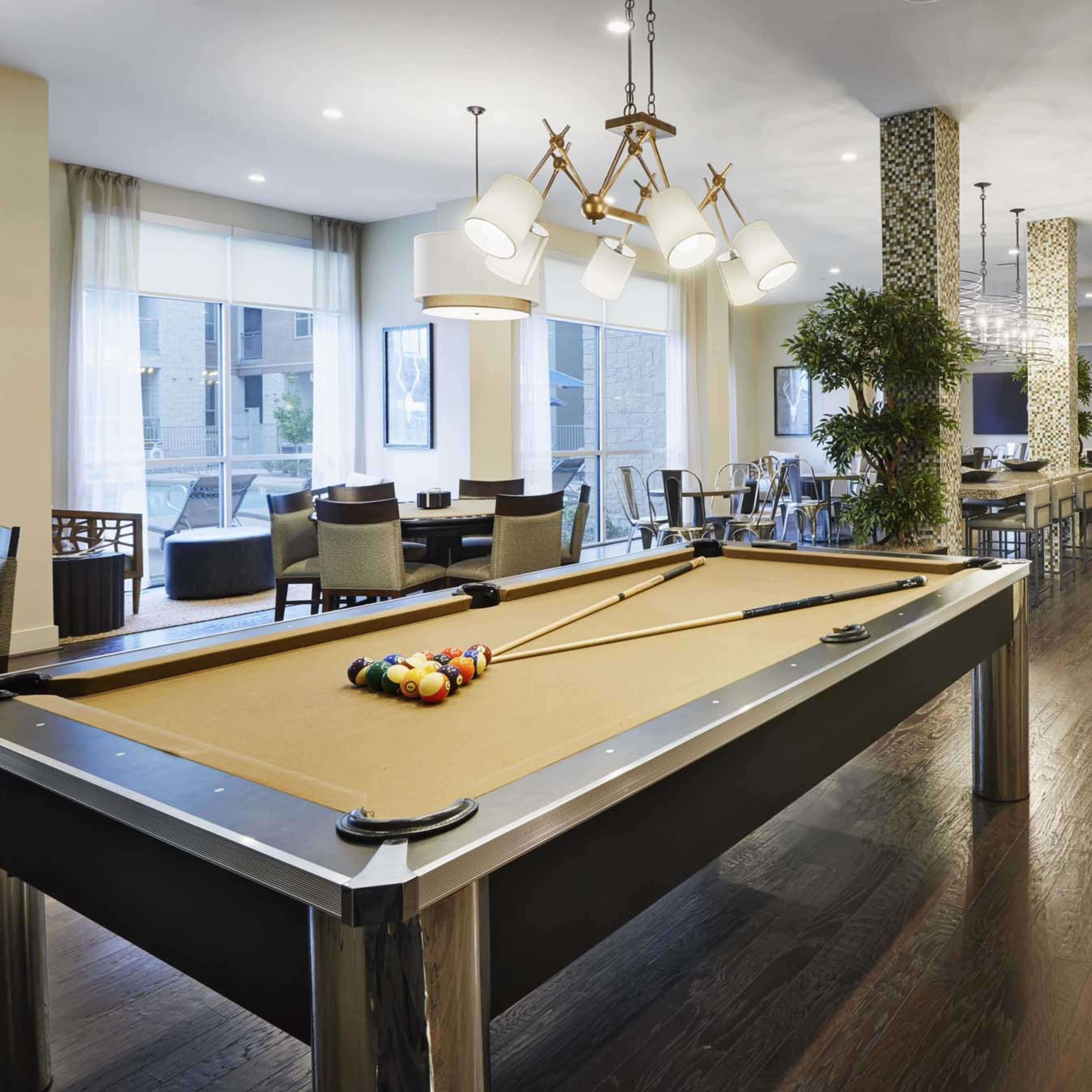 A spacious indoor area featuring a pool table, dining tables, and a modern kitchen setup.
