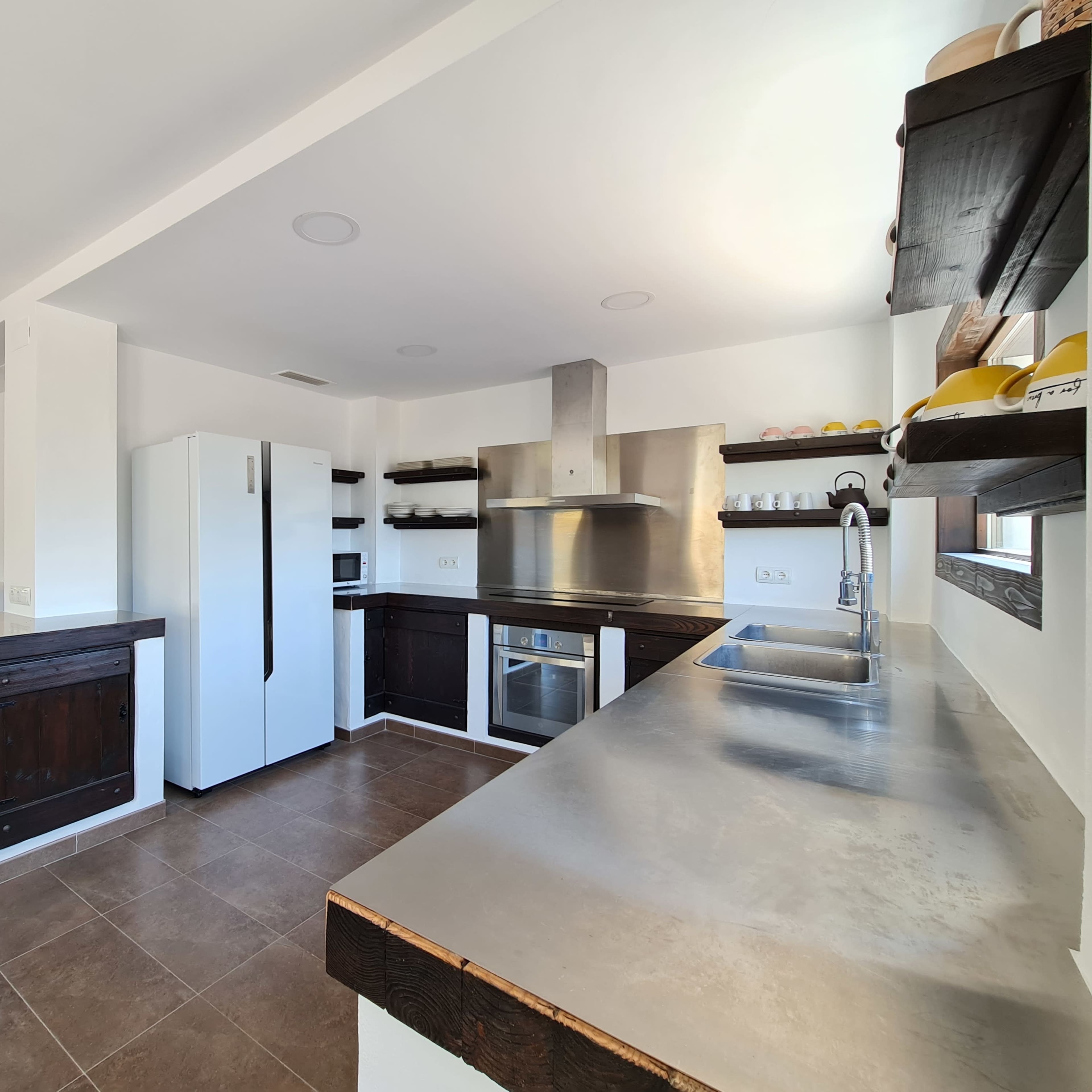 A modern kitchen with stainless steel appliances, a gray countertop, and an adjacent seating area with red cushions.