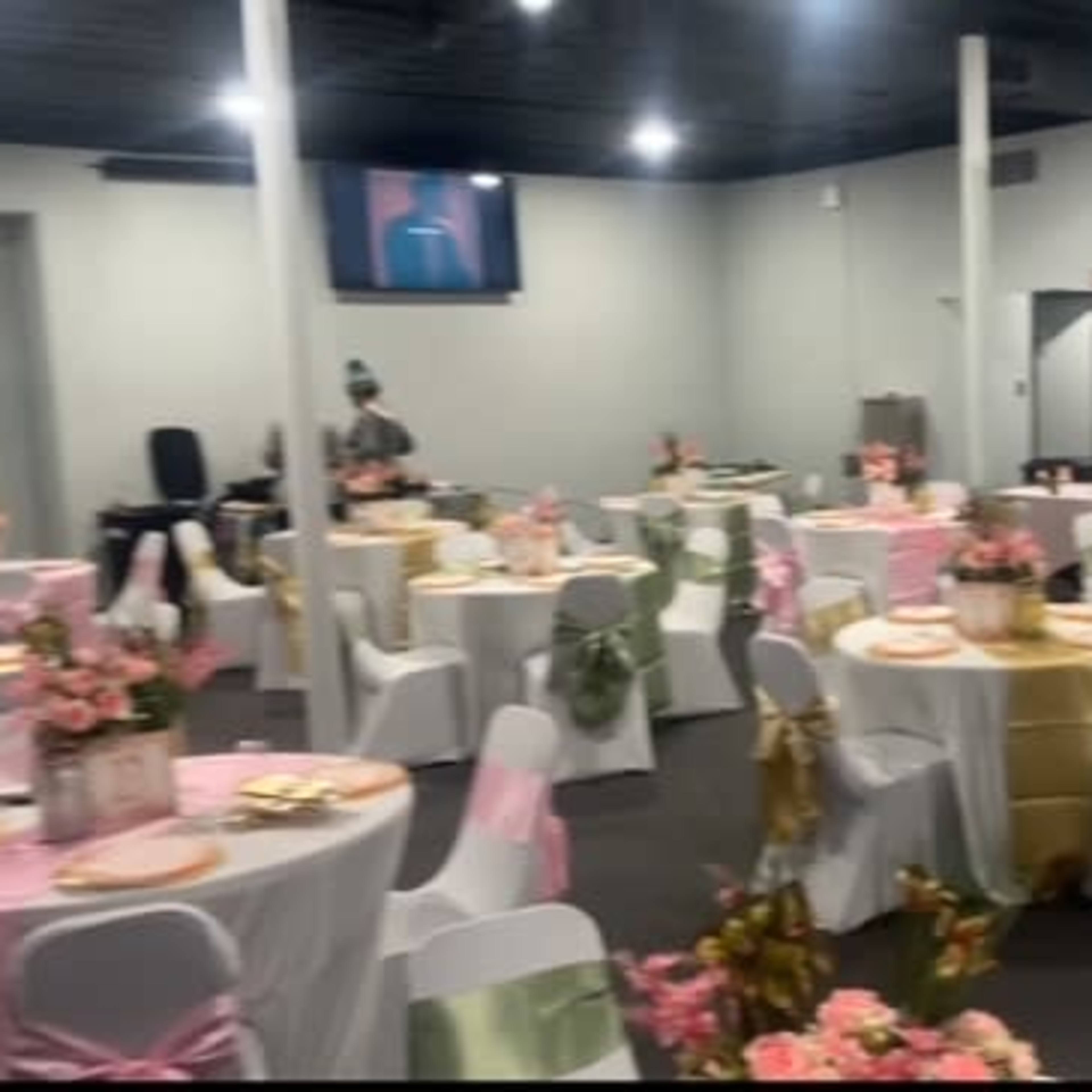 A banquet hall set up with several round tables decorated with pink and gold tablecloths, each featuring floral centerpieces.