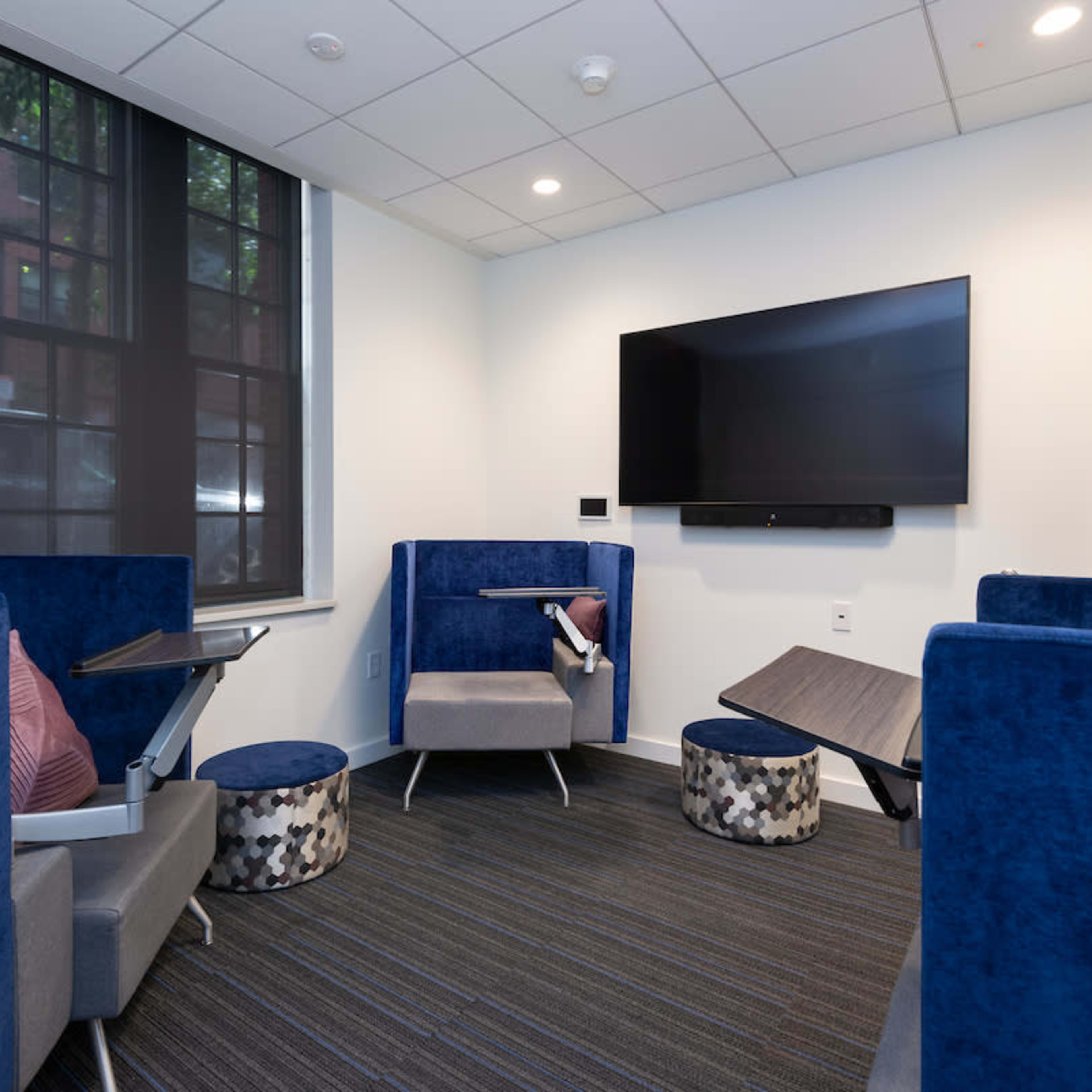 A small lounge area with blue upholstered seating, small tables, and a wall-mounted television.