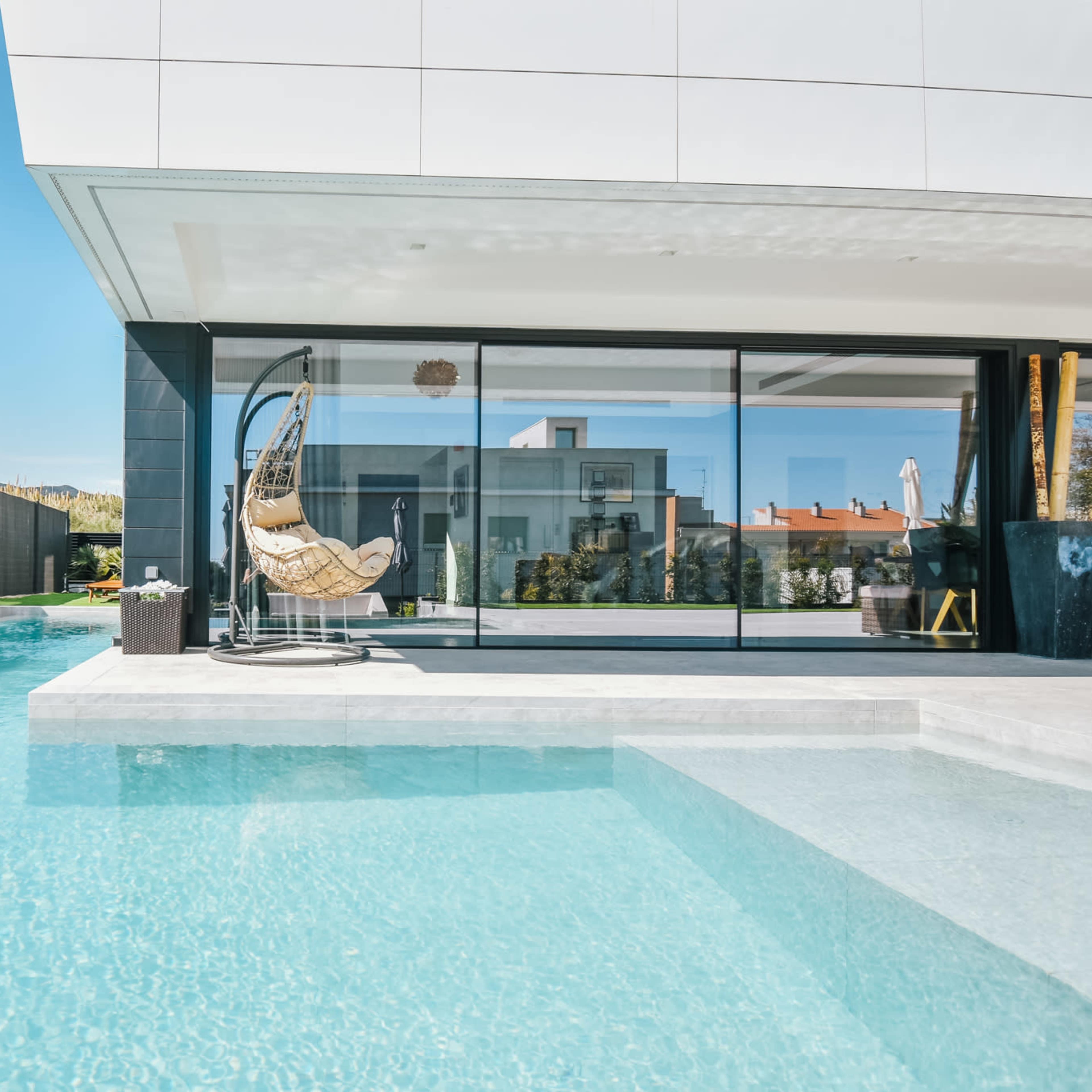 A modern house with a sleek white exterior, large glass windows, and a pool in the backyard.