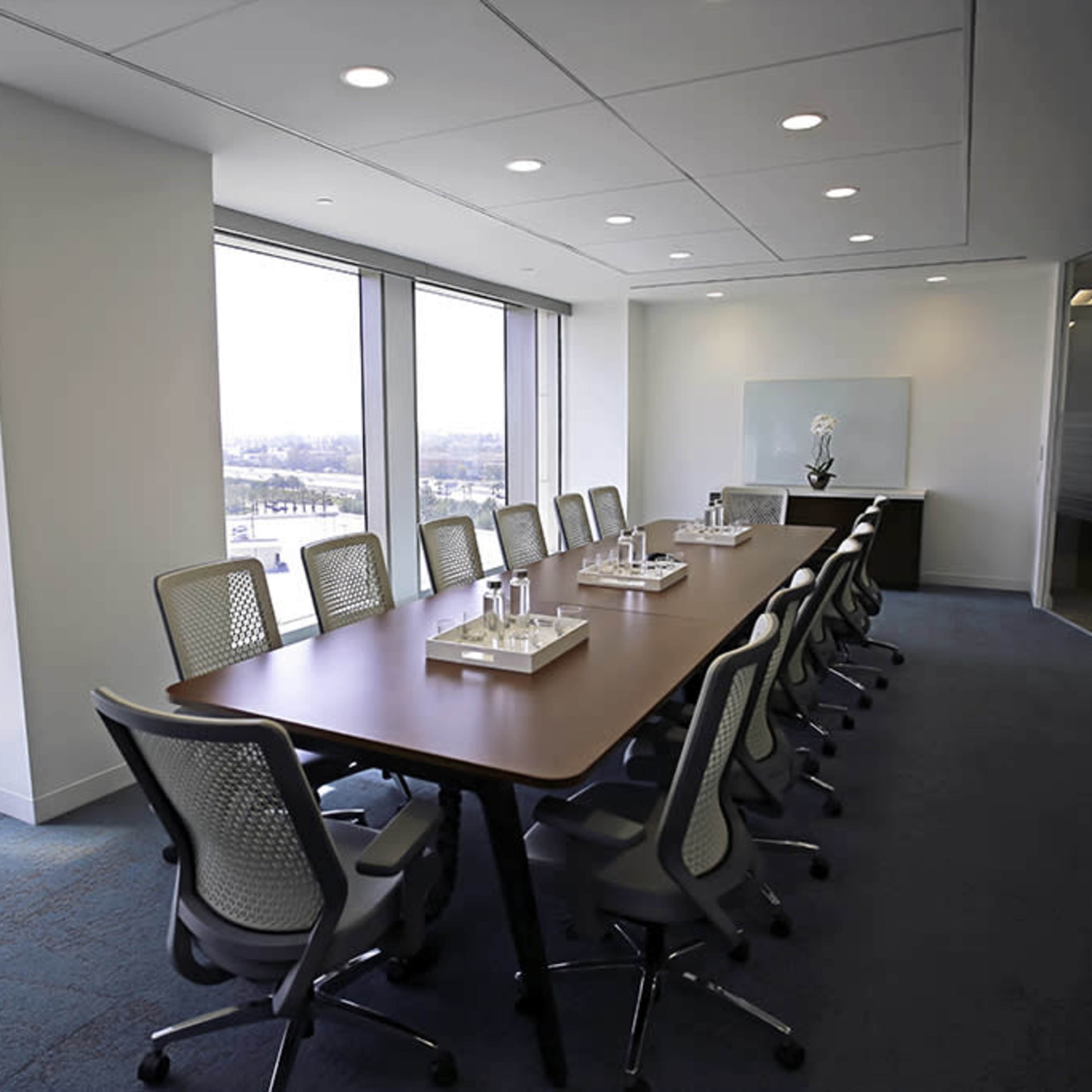 A modern conference room features a long table with chairs, large windows providing natural light, and a minimalist decor.