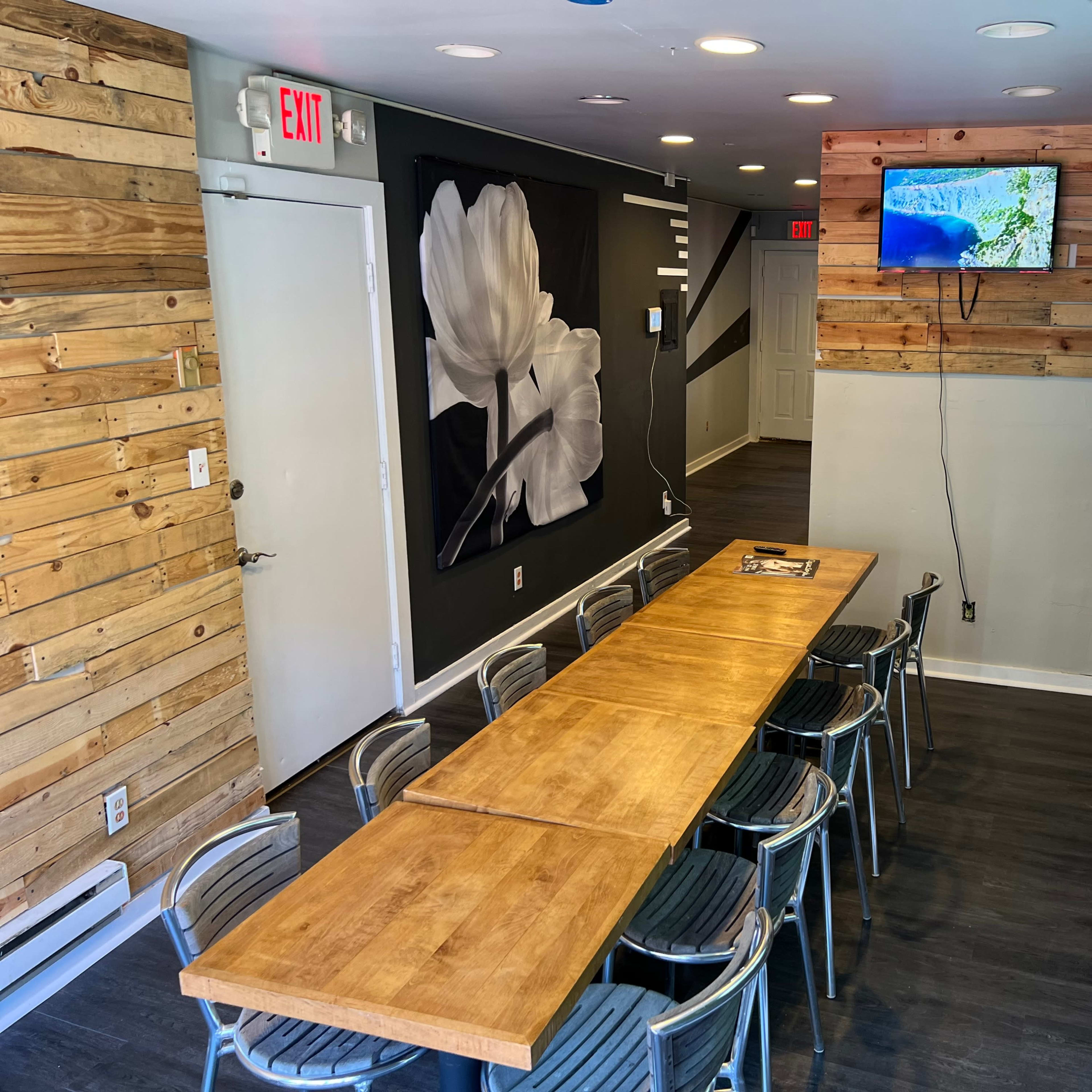 A modern meeting room with a long wooden table surrounded by metal chairs, a wall adorned with a floral mural, and a television mounted on a green, plant-covered wall.