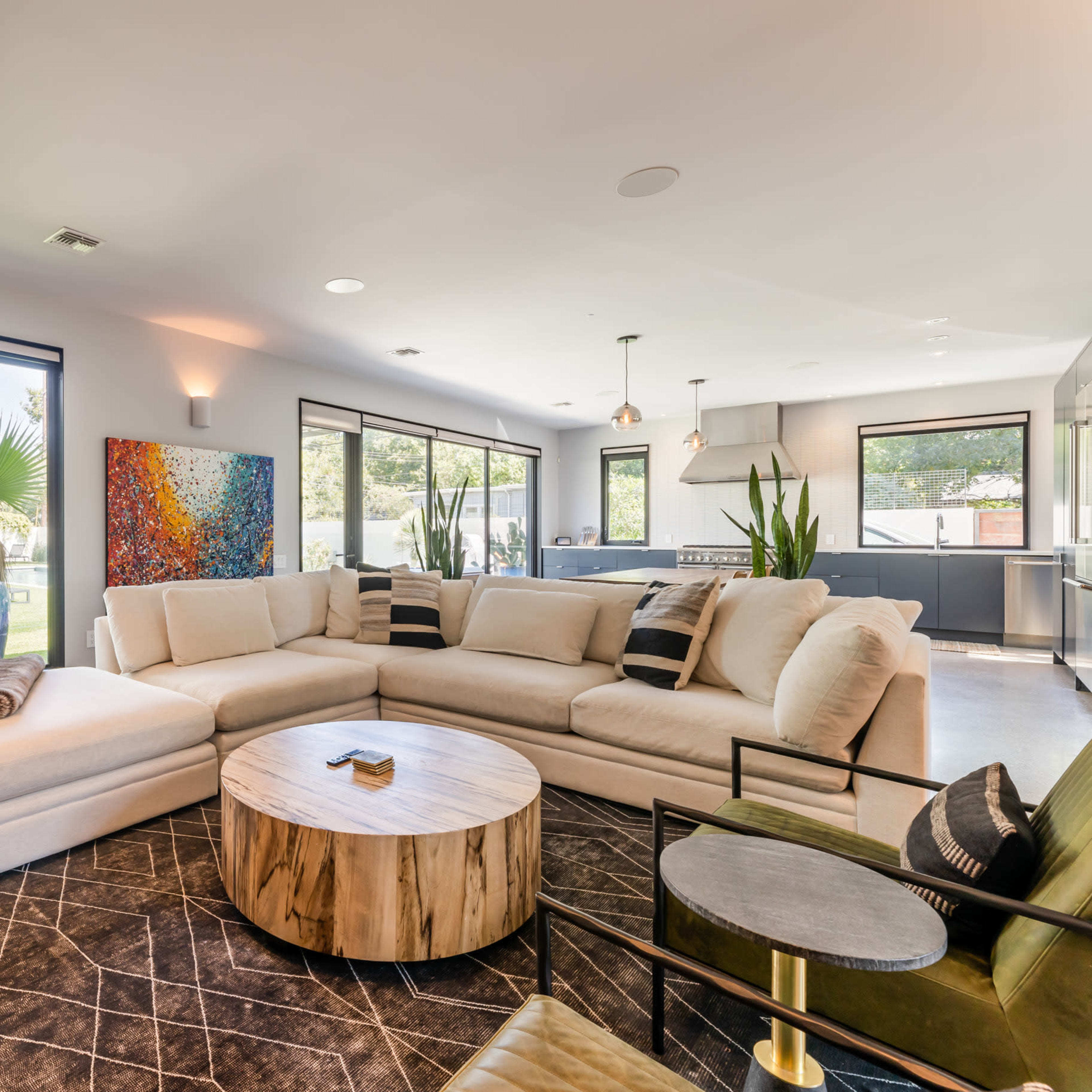 A modern living room with a large sectional sofa, a circular wooden coffee table, and large windows providing a view of the outdoors.