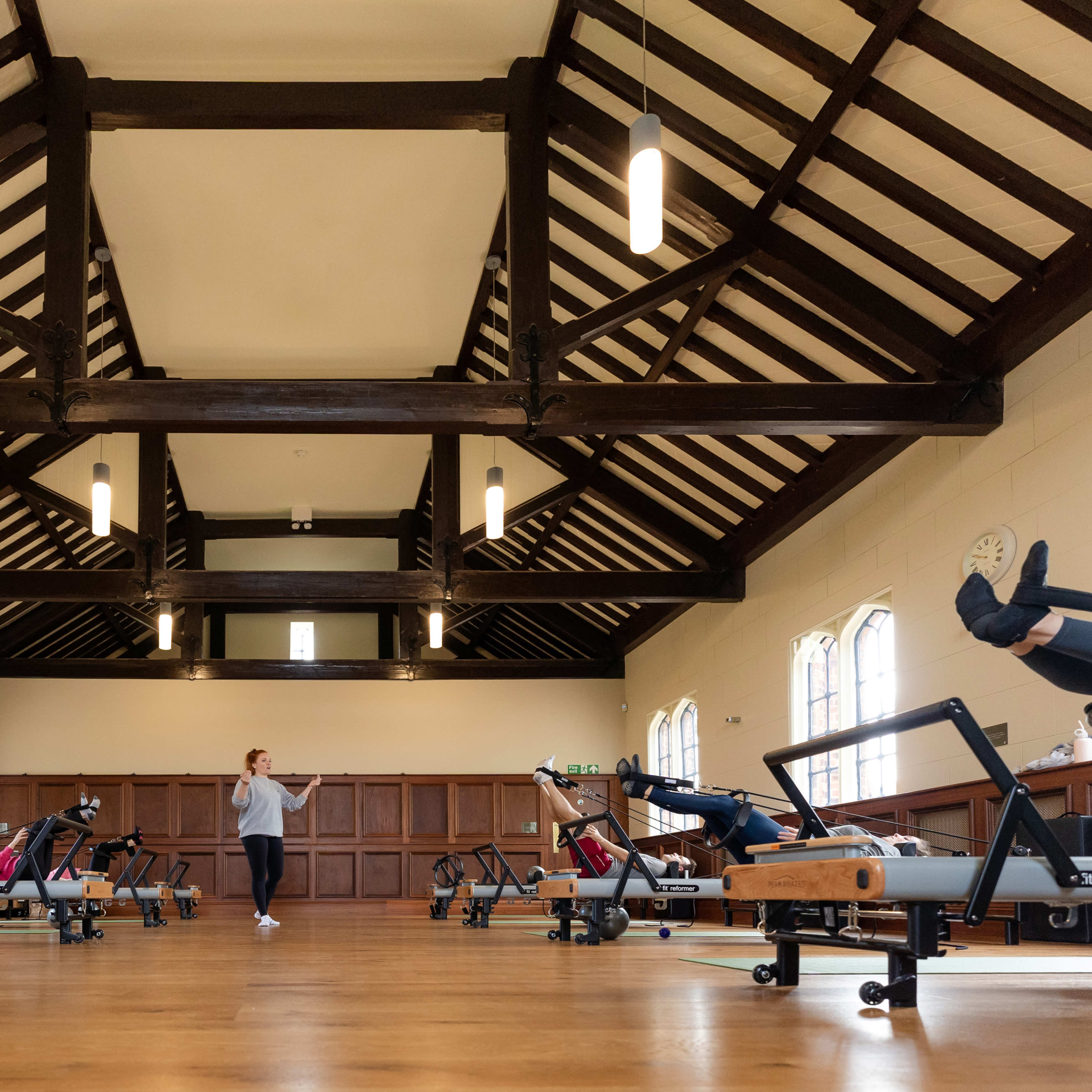 A spacious fitness studio features several reformer machines arranged in rows beneath a high, beamed ceiling.