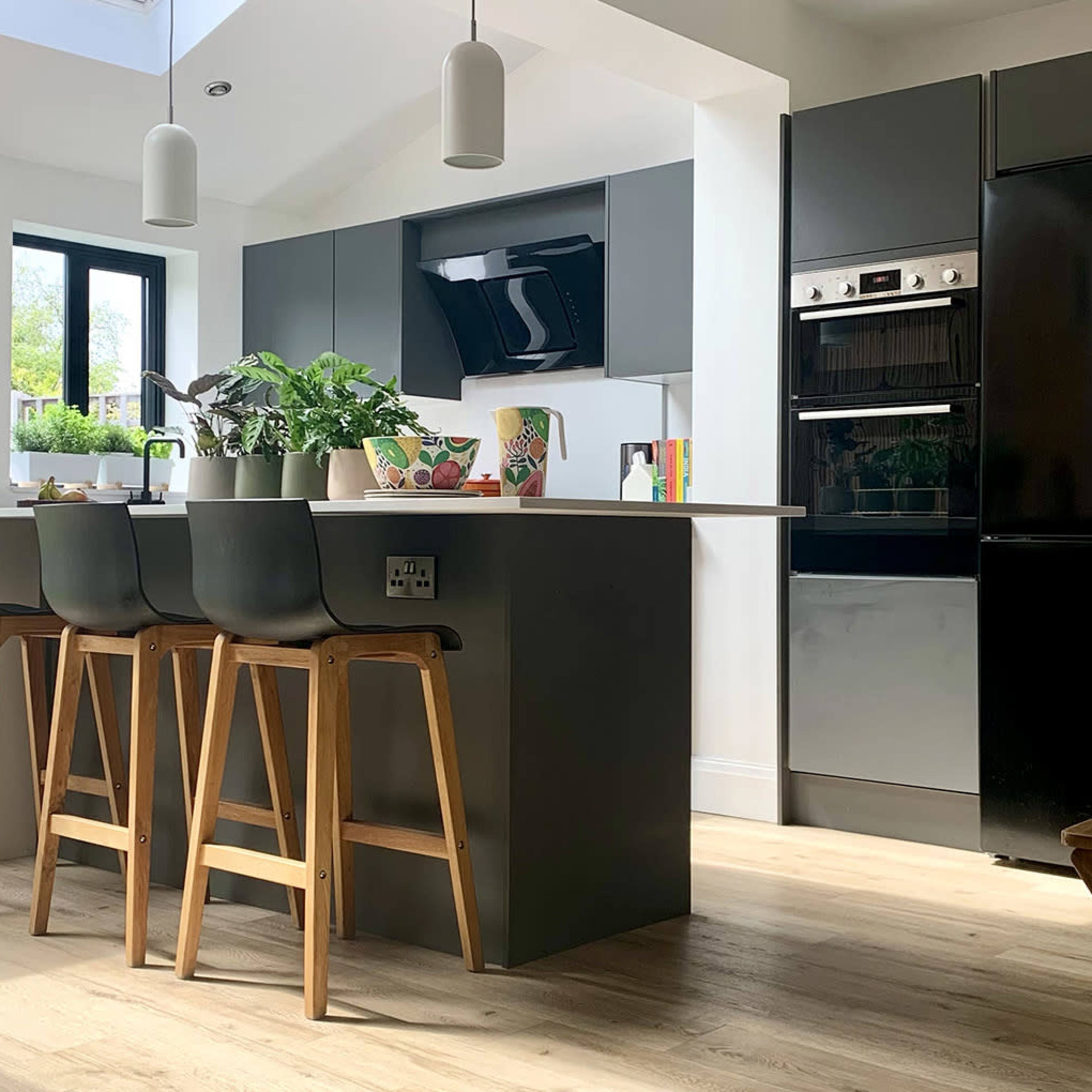 A modern kitchen features dark cabinetry, a dining area with wooden stools, and large windows allowing natural light.