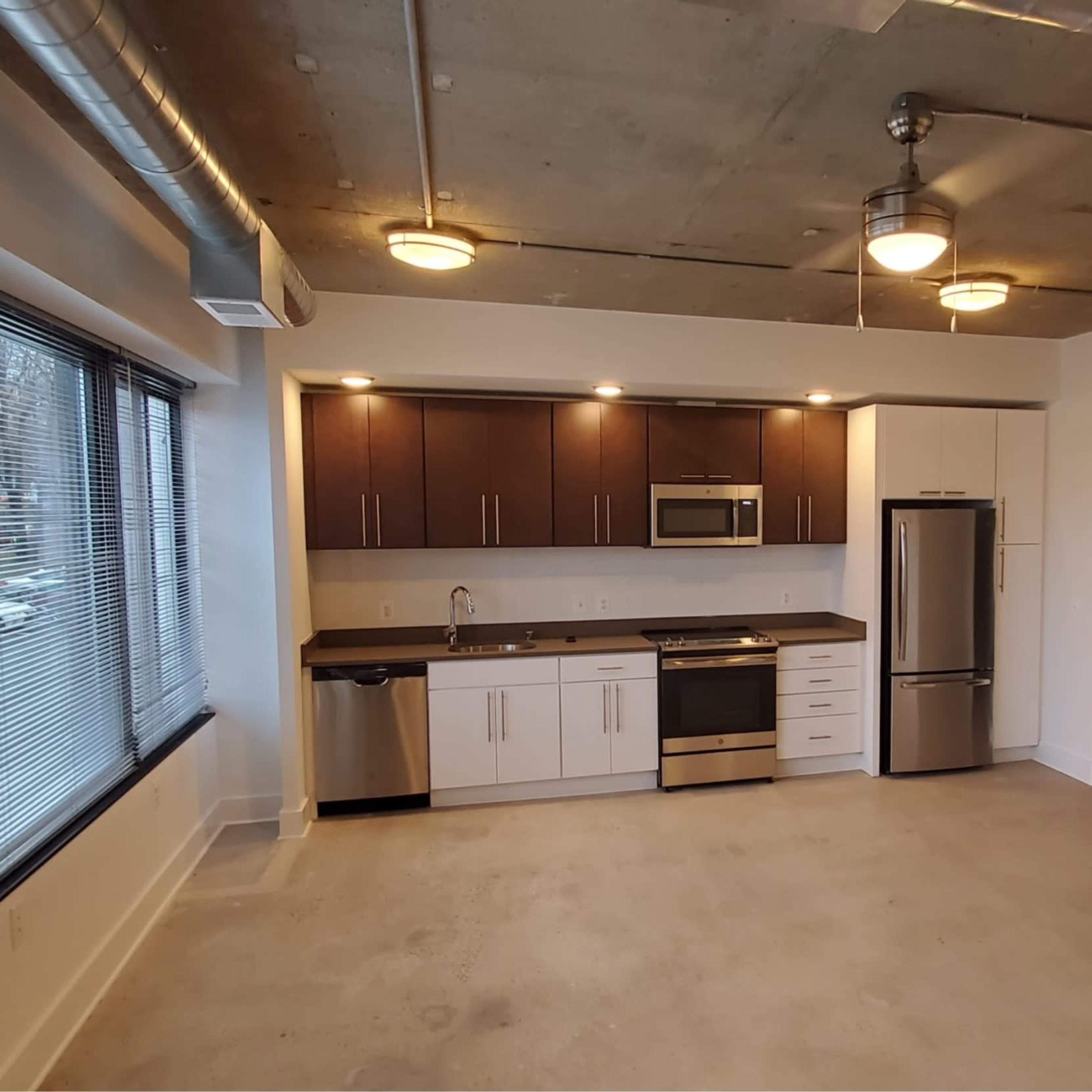 A modern, minimalistic apartment interior featuring a kitchen area with wooden cabinets, stainless steel appliances, and an open living space.