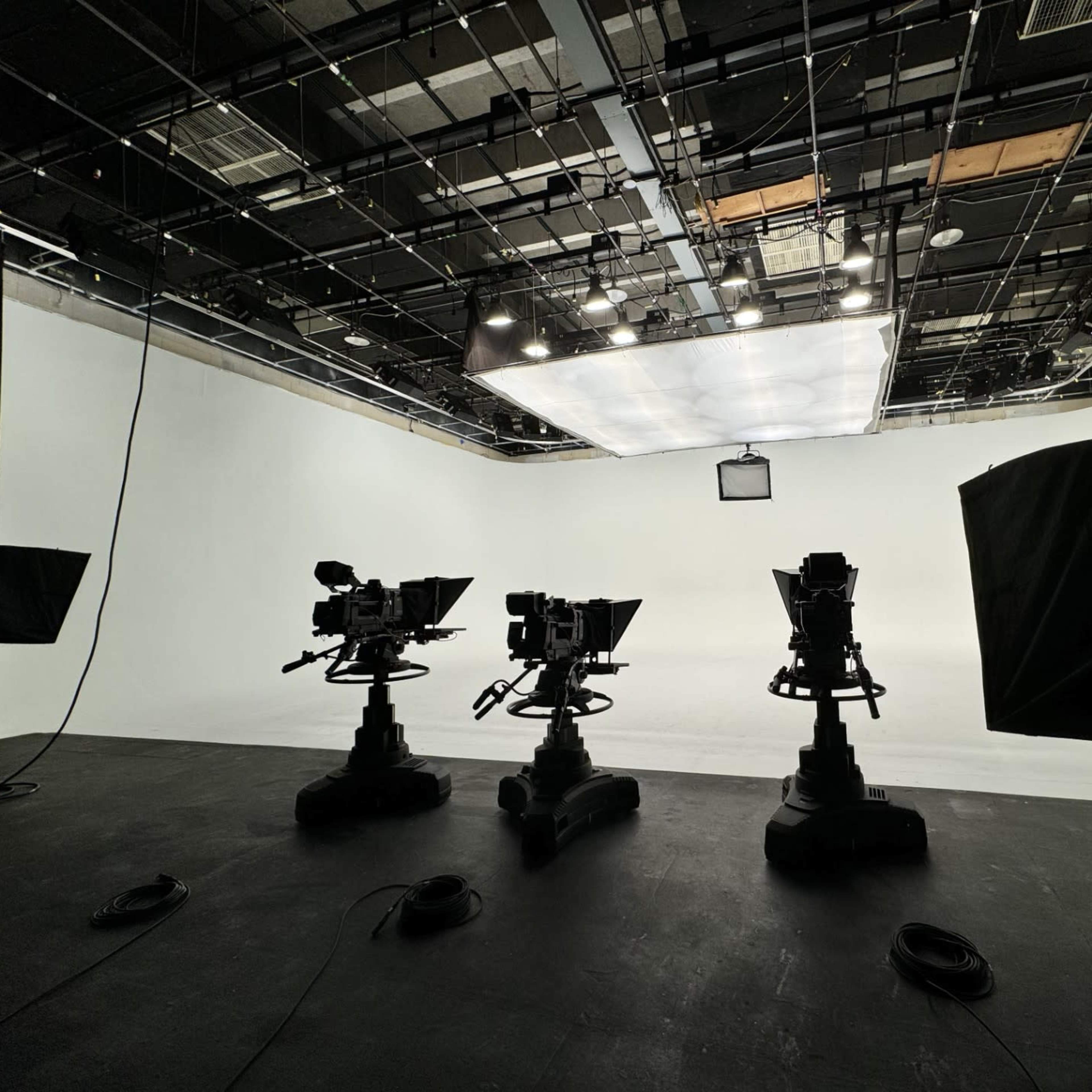 A television studio with three camera setups facing a blank white backdrop.