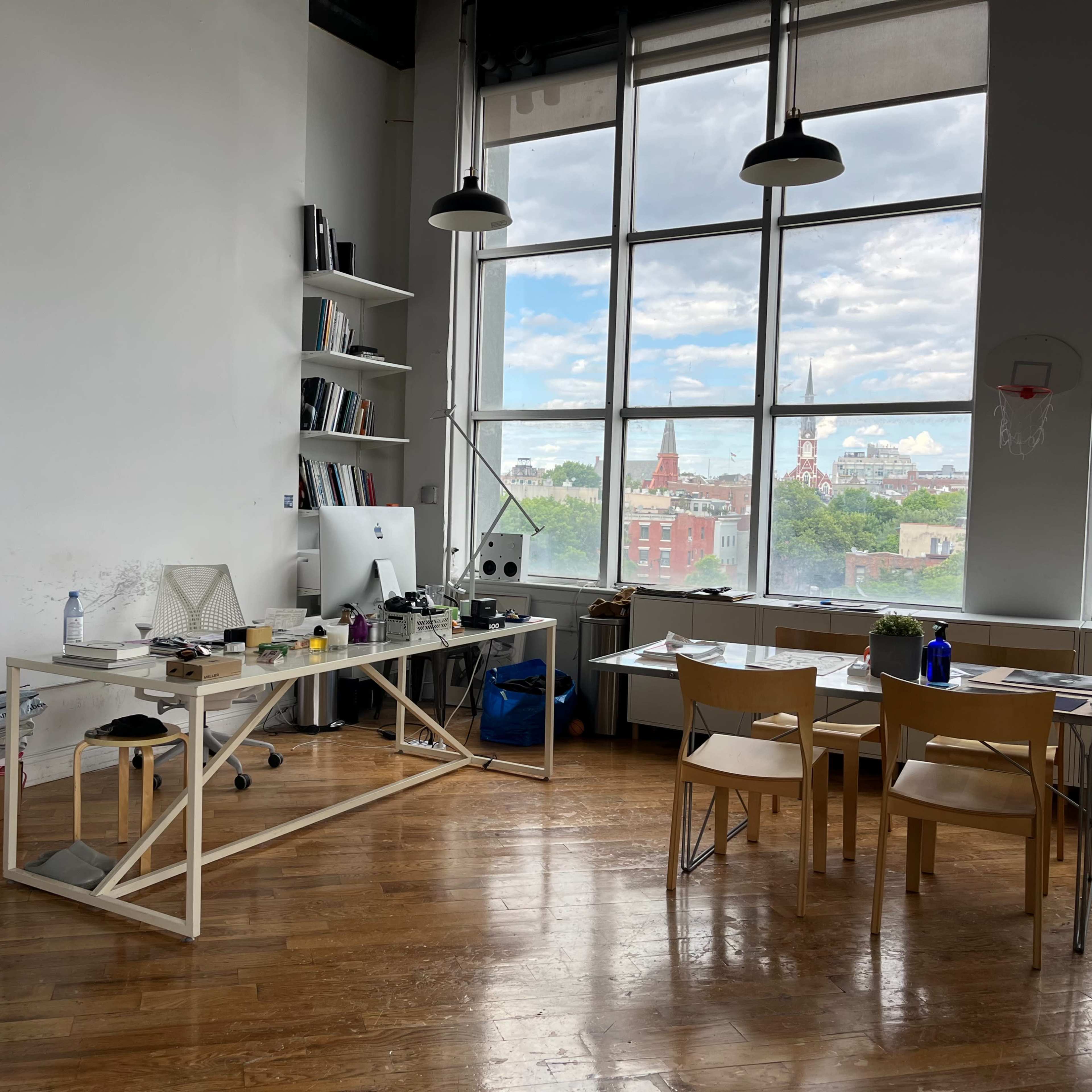 A spacious, bright office with a large window offering a view of a city skyline, featuring a minimalist desk and several chairs.