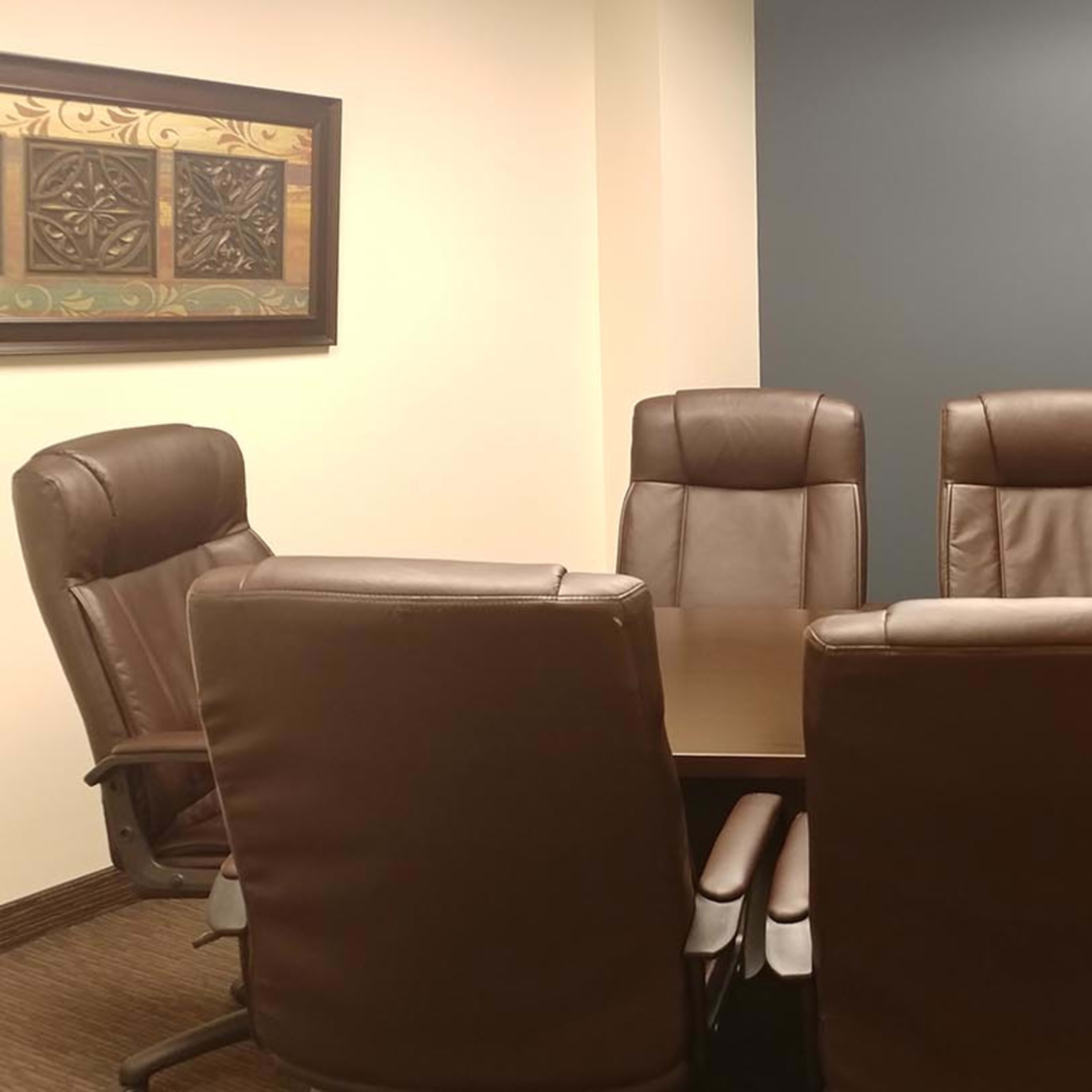 A conference room features a circular table surrounded by five leather office chairs and a dark blue wall.