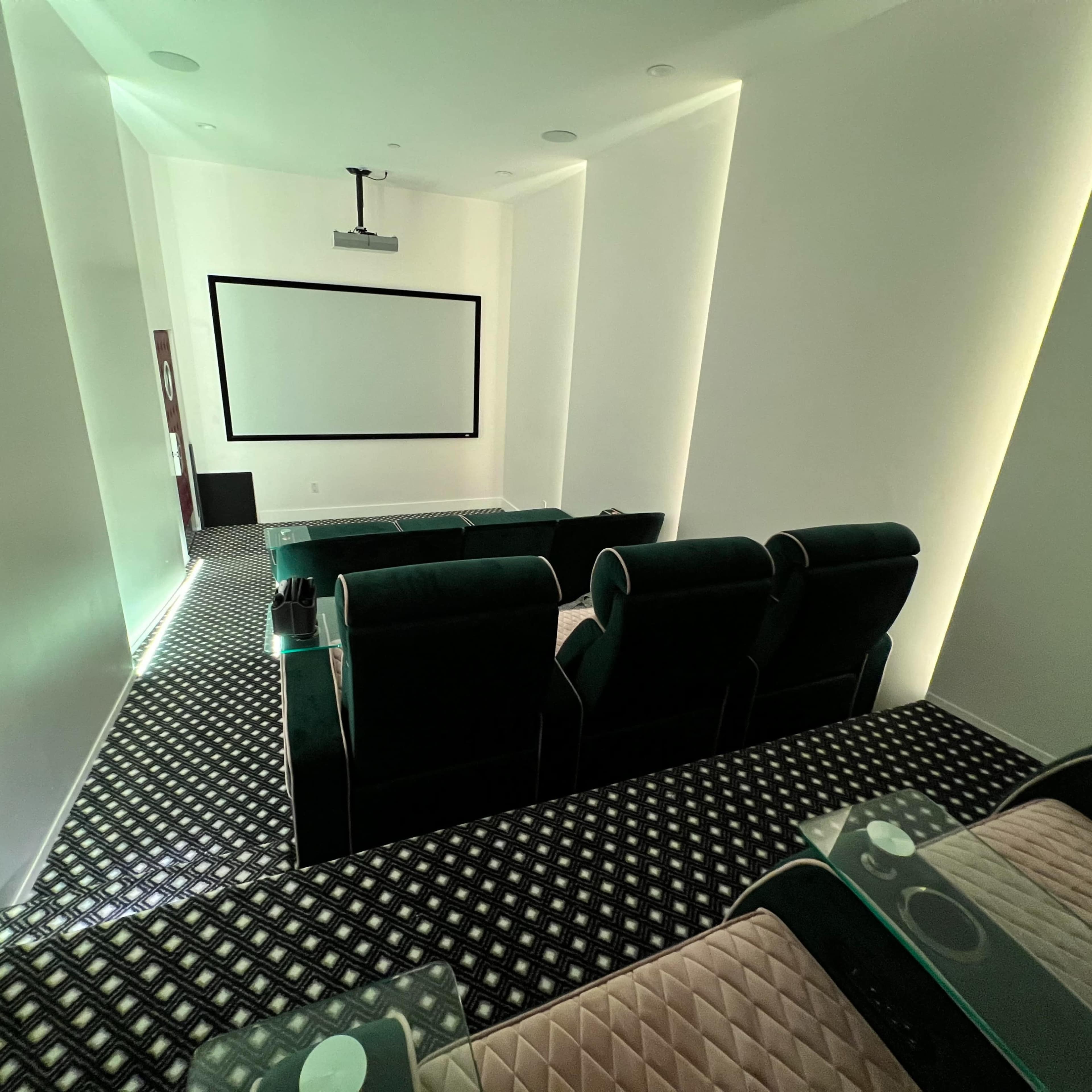 A home theater room with dark seating facing a blank screen, surrounded by illuminated walls and a patterned floor.