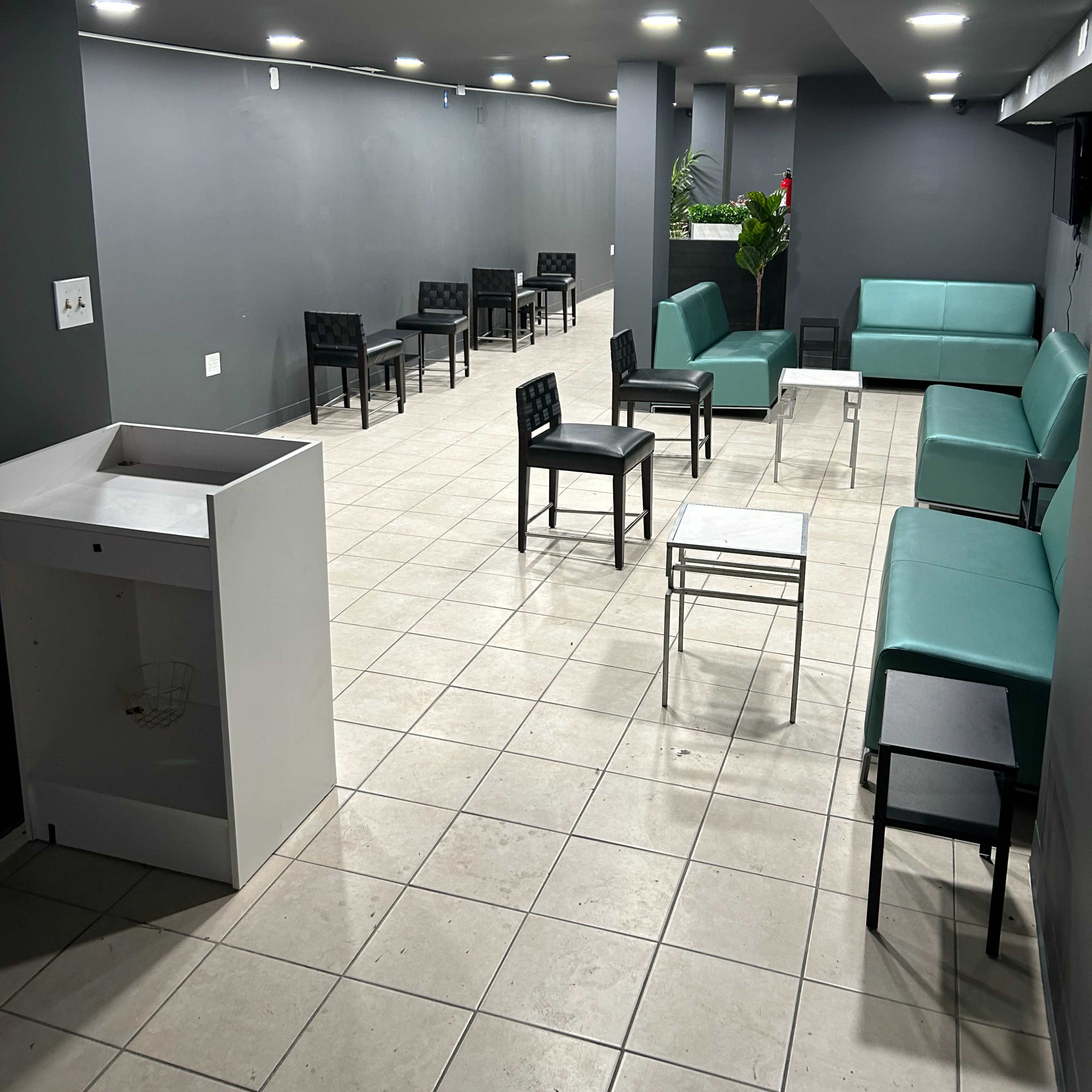 A spacious, modern lounge area featuring several chairs and couches arranged along the walls, with a few tables scattered throughout the tiled floor.