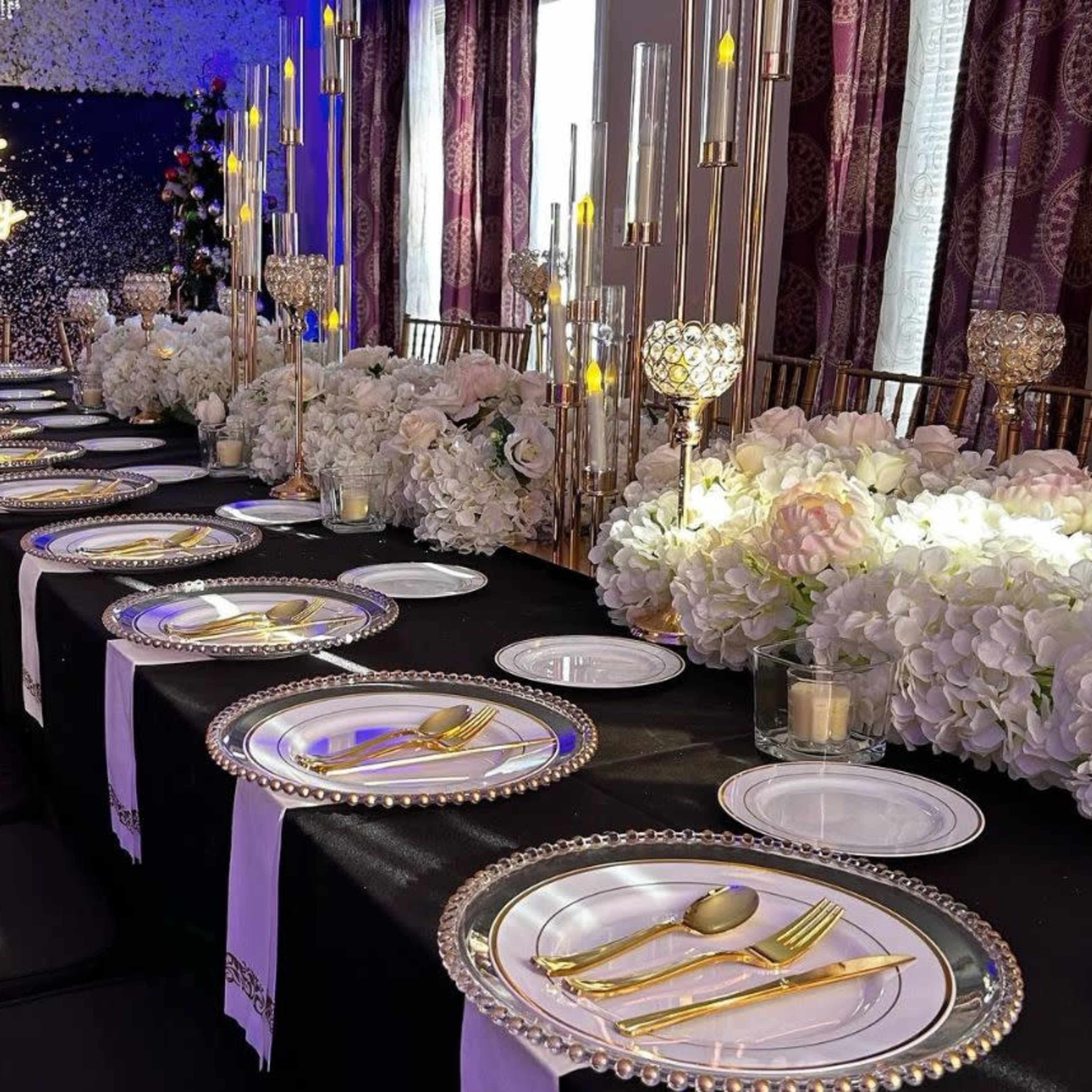 A long dining table is set for a birthday celebration, decorated with white flowers, elegant tableware, and gold accents.