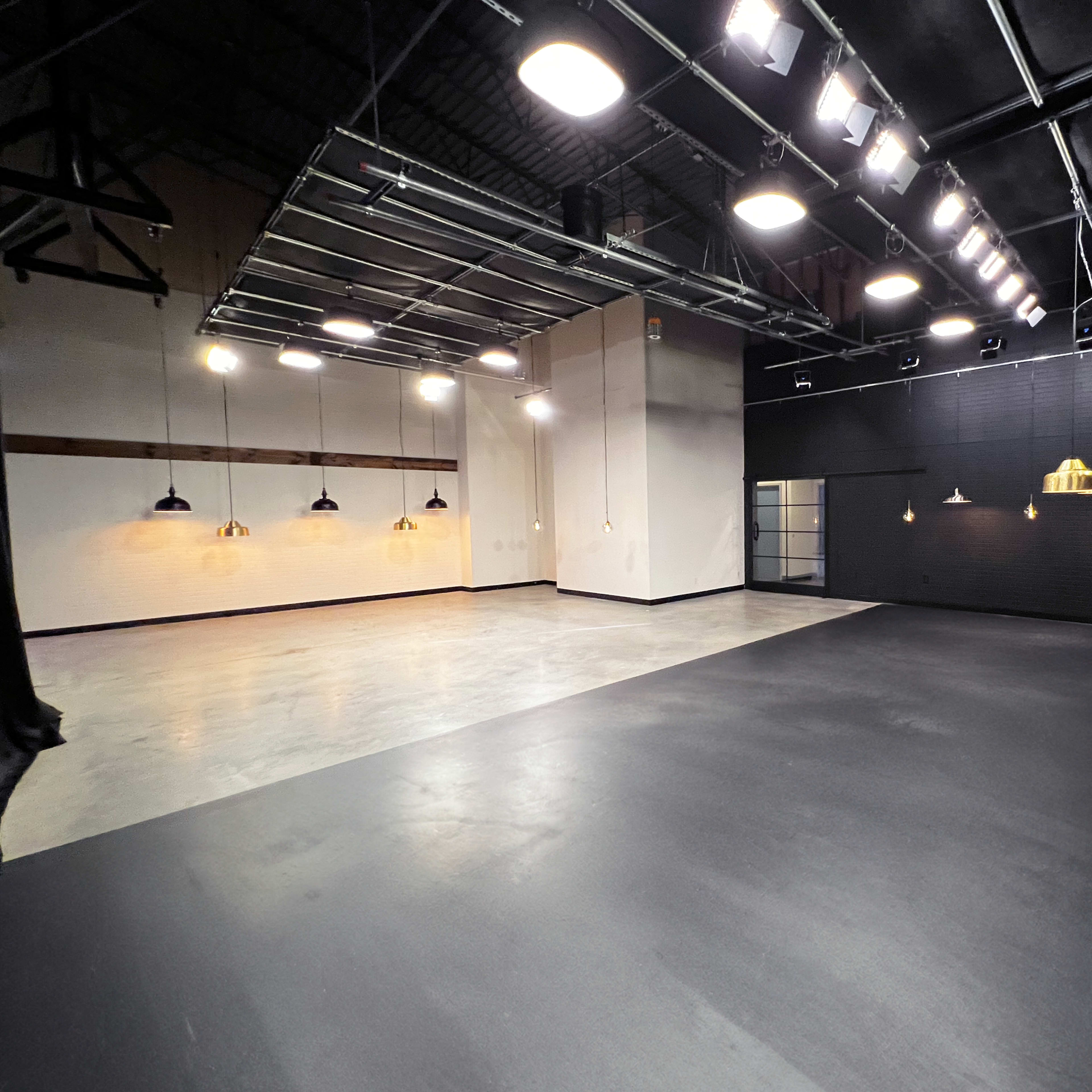 A spacious interior studio with black flooring, bright overhead lights, and pendant lights hanging from the ceiling.