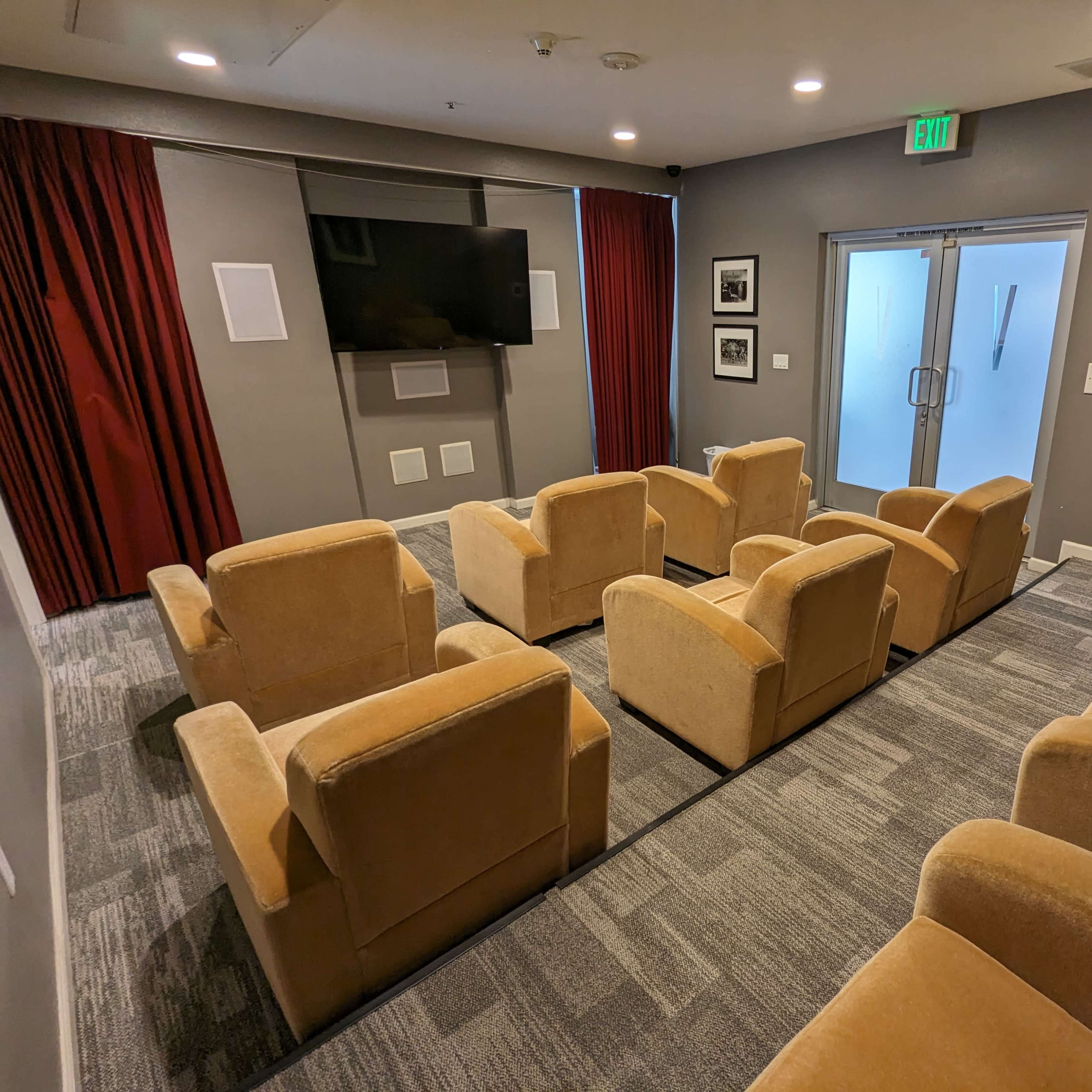 A small, modern theater room with several beige chairs arranged in rows facing a wall-mounted television.