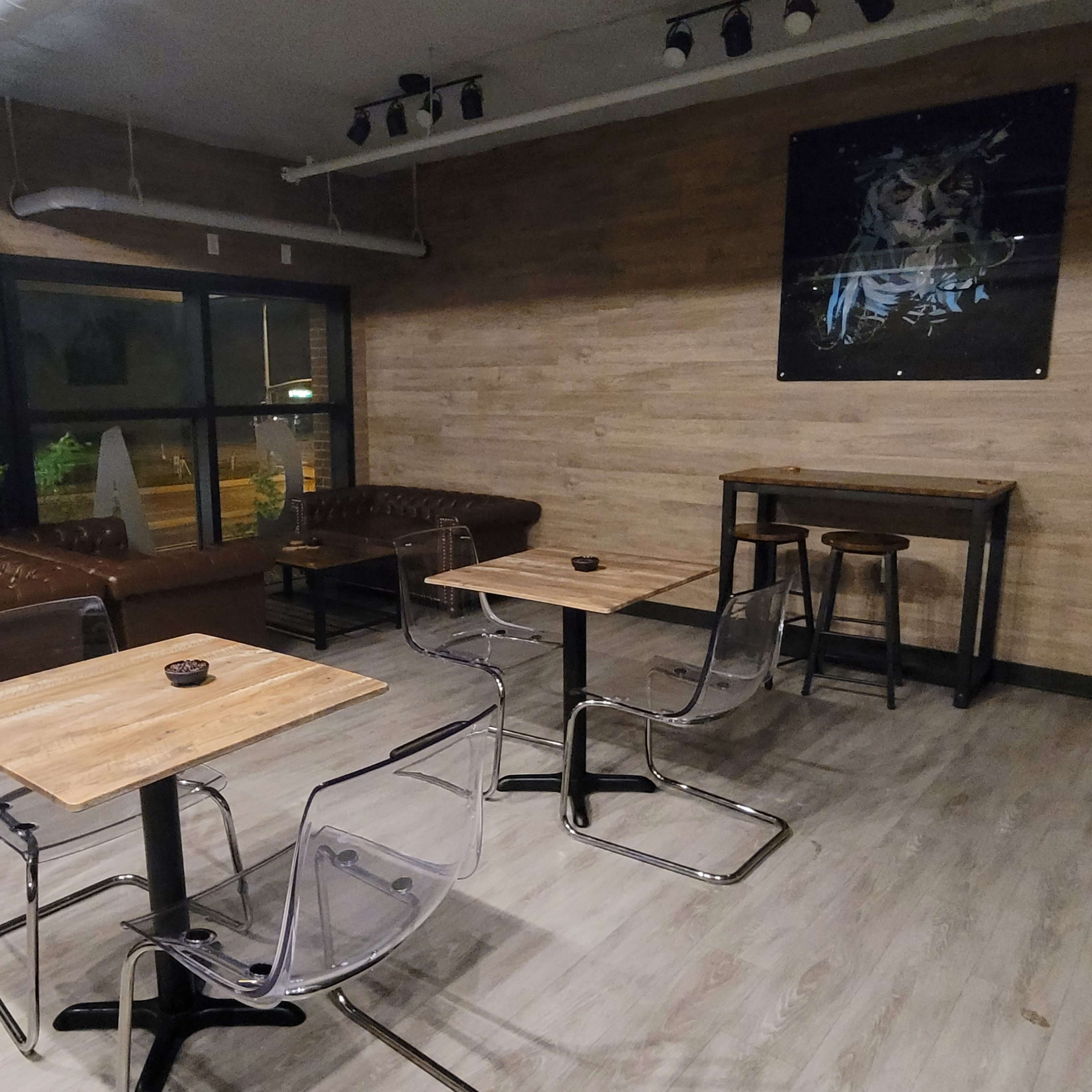 A modern cafe interior with two leather couches, several clear acrylic chairs around wooden tables, and a framed artwork on the wall.