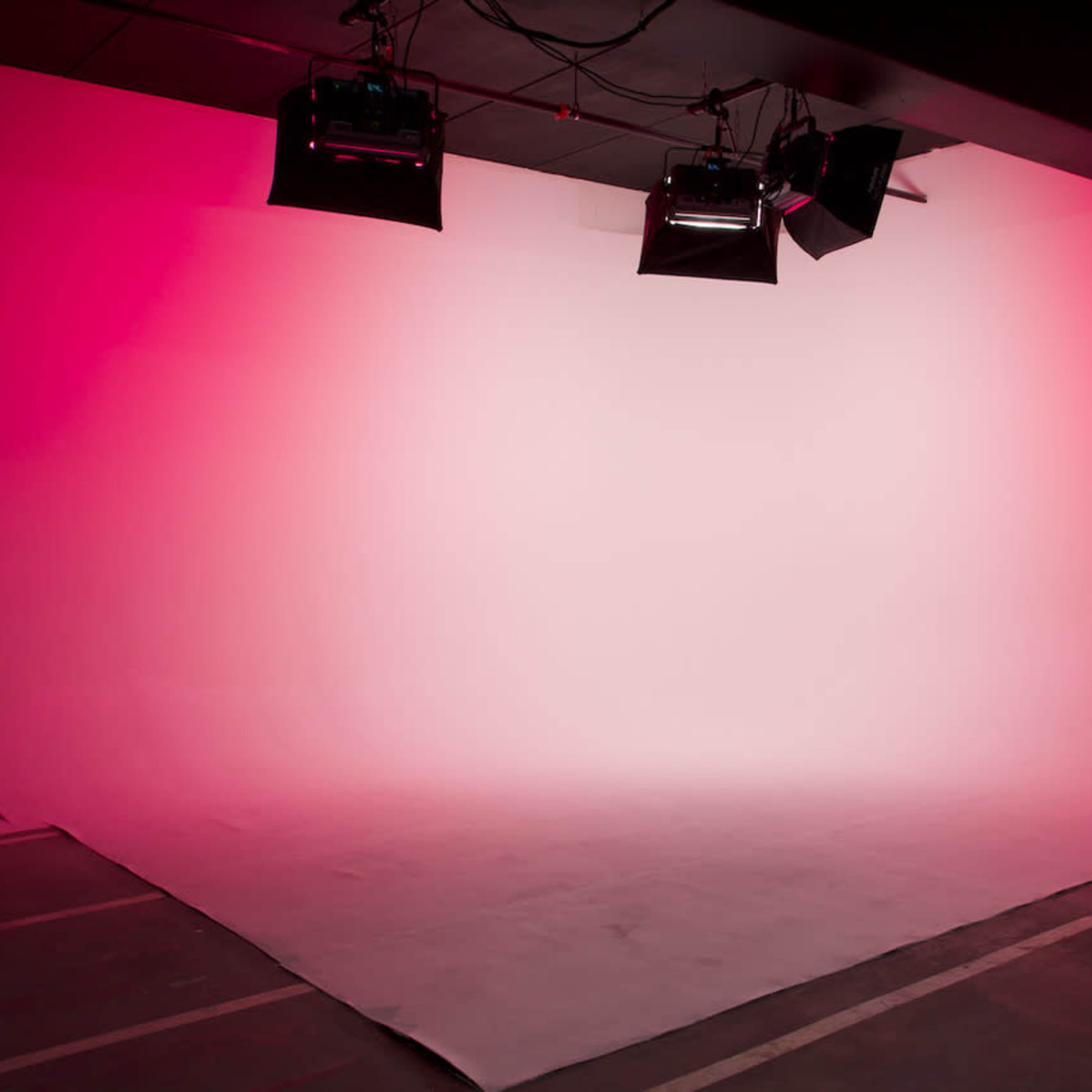 A photography studio features a blank backdrop illuminated by overhead lights, creating a gradient effect.