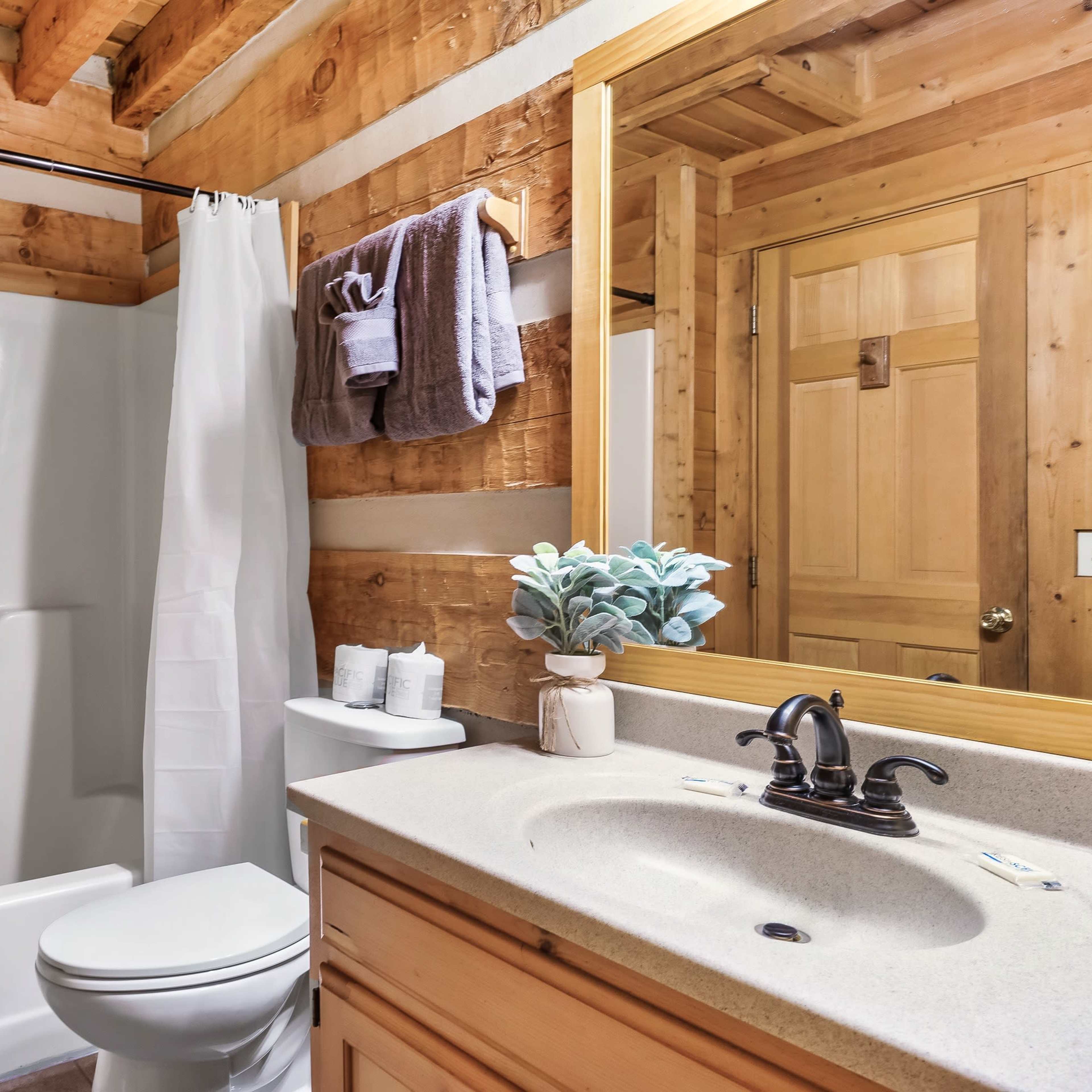 A bathroom featuring a shower/tub combo, a toilet, a sink with a countertop, wooden walls, and a mirror above the sink.