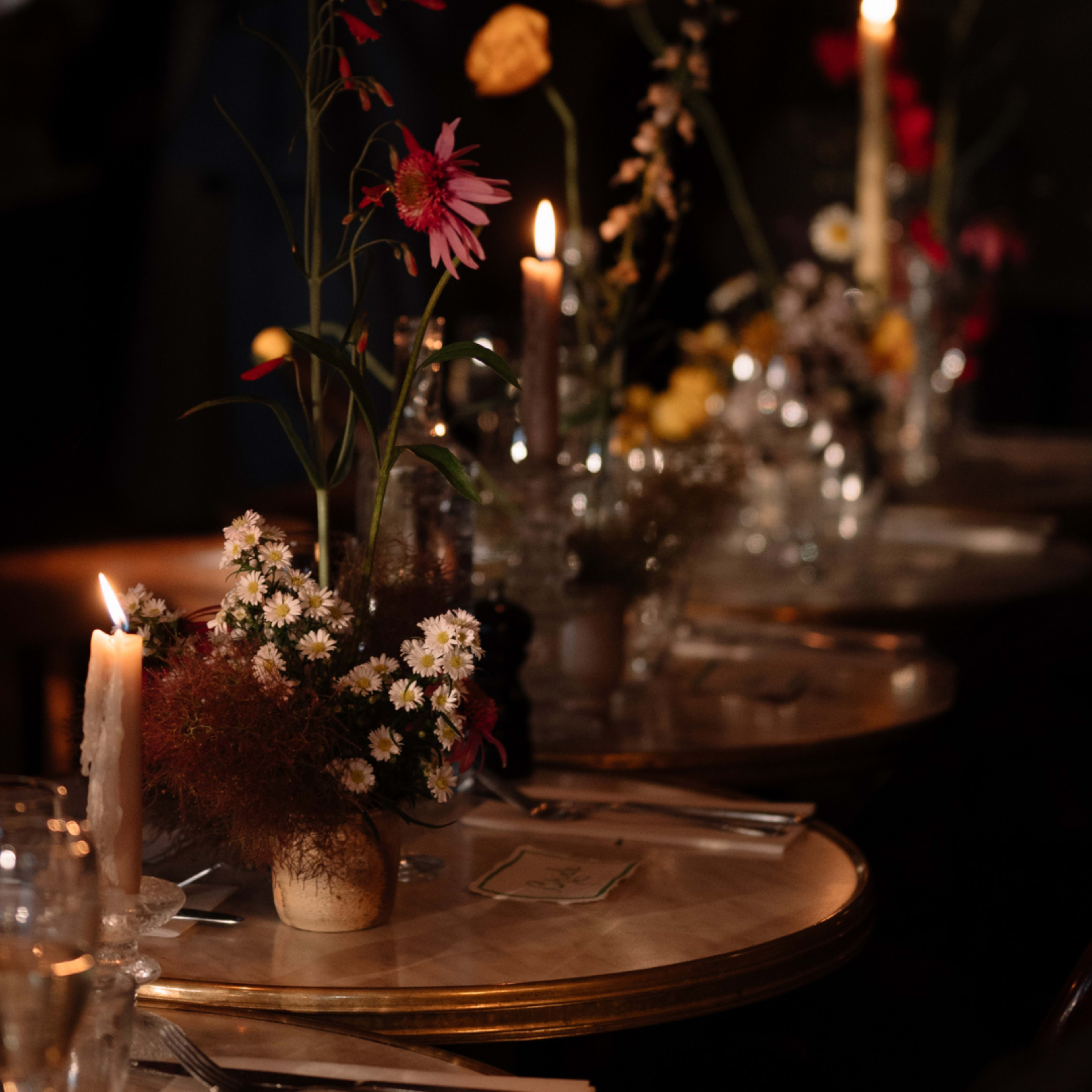 A dining table set with candles, floral centerpieces, and glassware in a dimly lit setting.