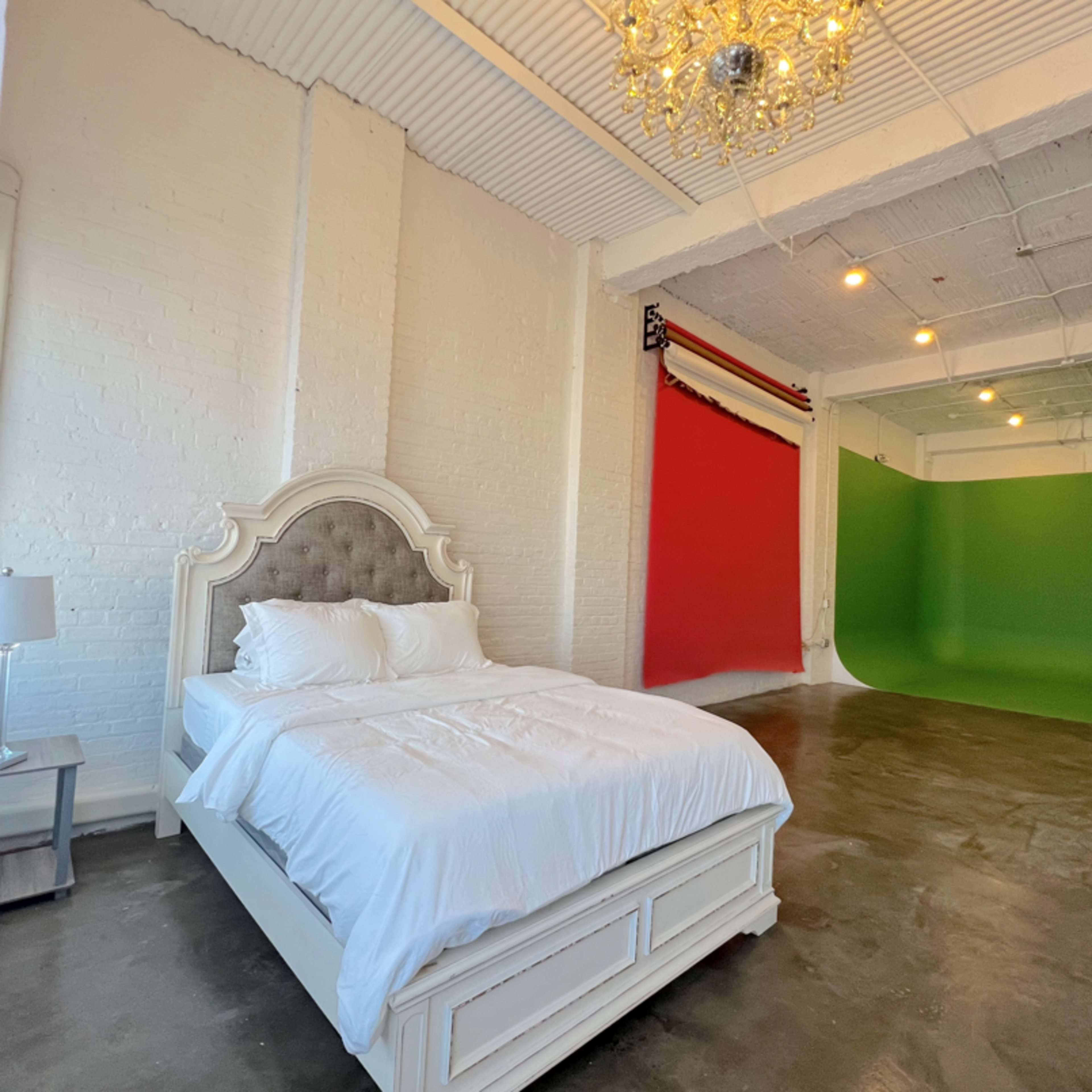 A bright bedroom features a white bed with plush bedding and a backdrop of red and green walls in the background.