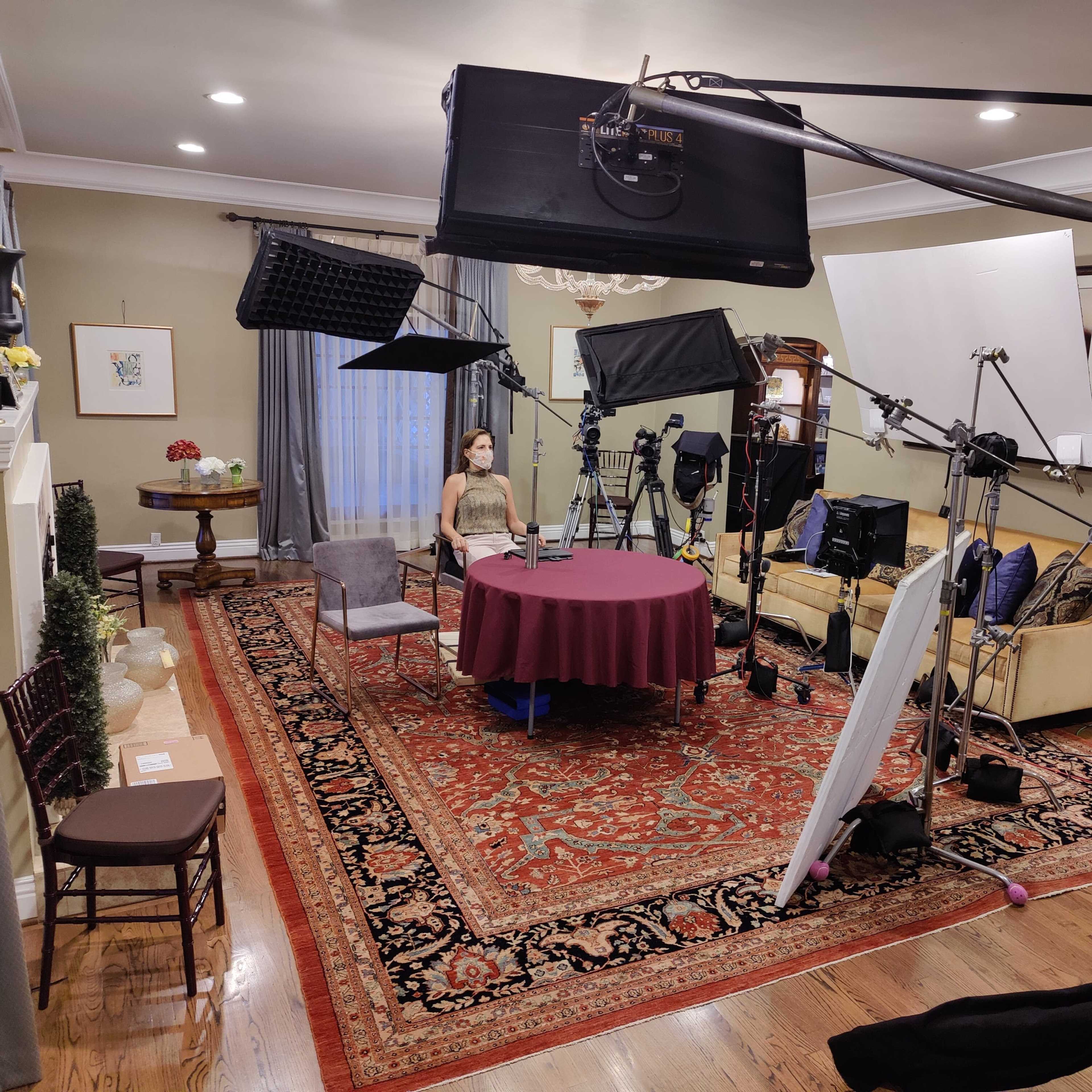 A well-equipped filming set featuring a circular table with a tablecloth, surrounded by various lighting and camera equipment in a living room.