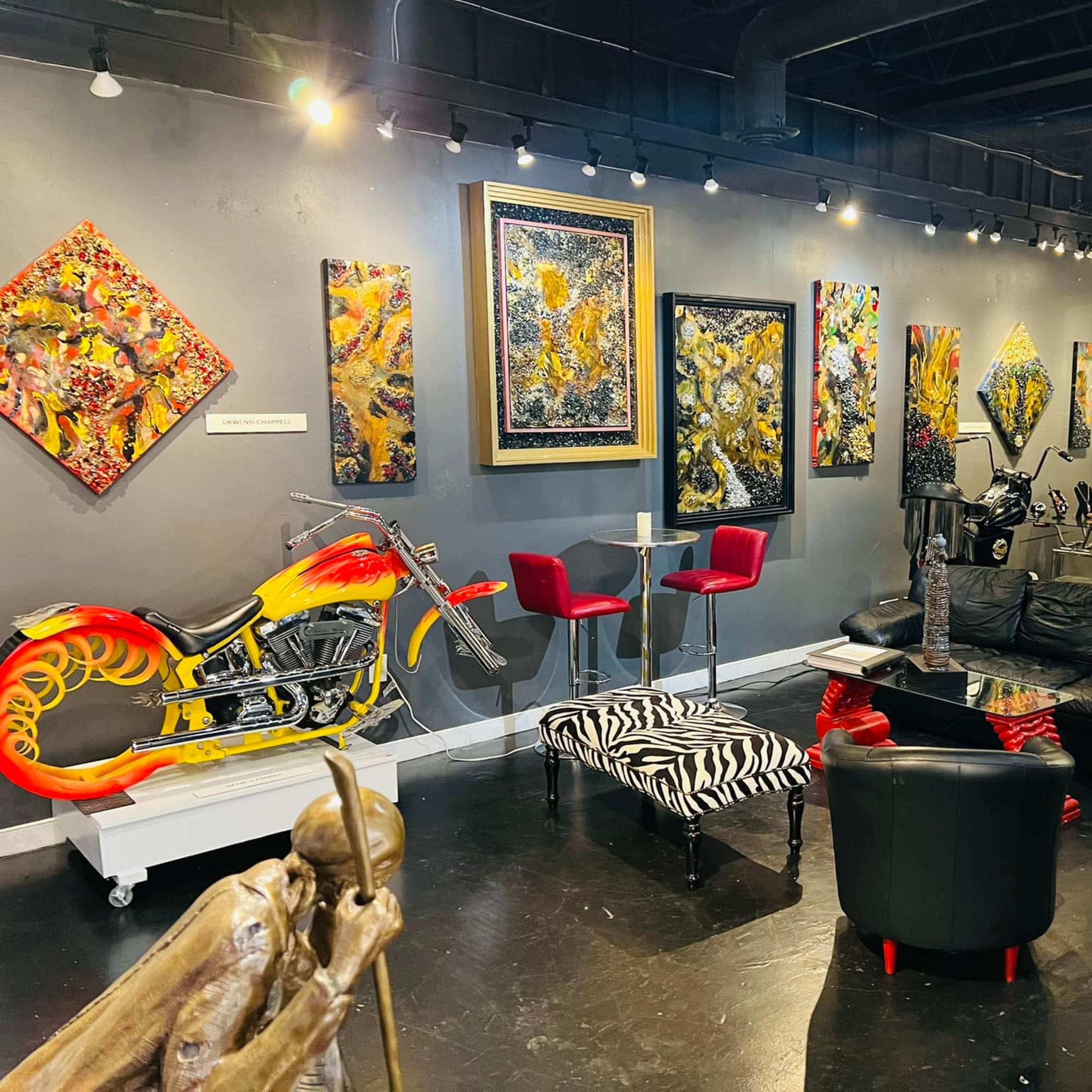 An art gallery featuring colorful paintings on the walls, a motorcycle sculpture, and seating areas with modern furniture.