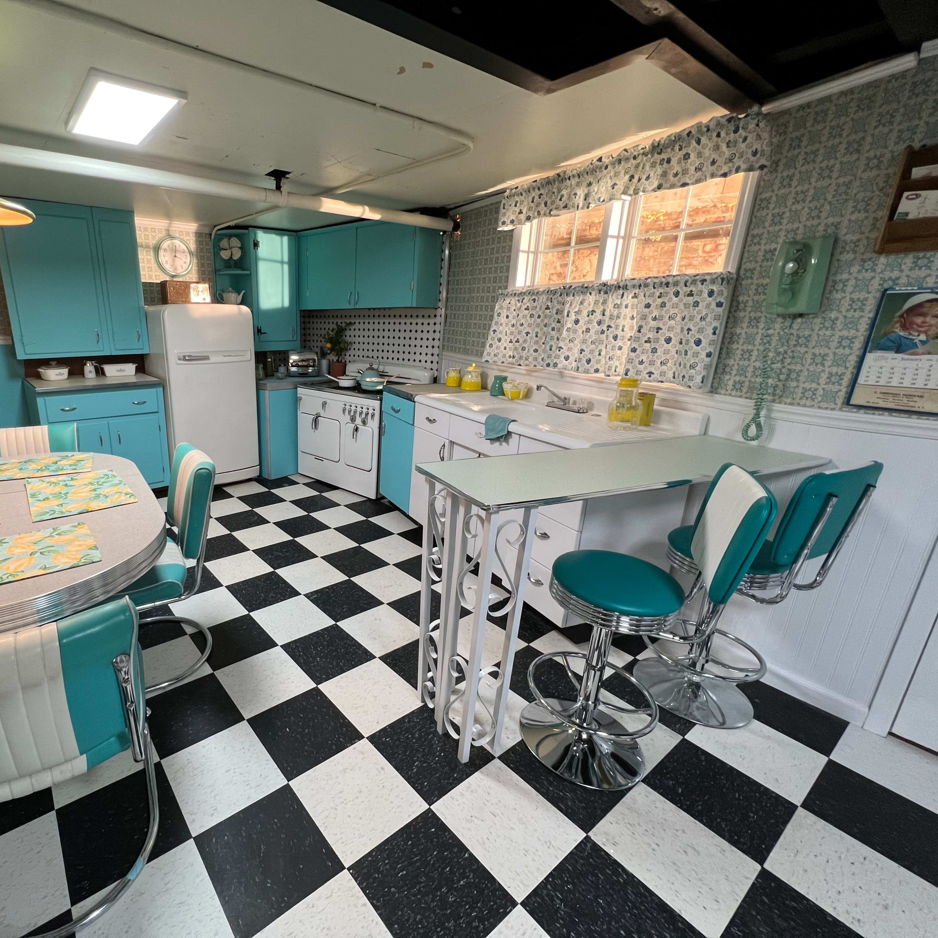 A retro-style kitchen with turquoise cabinets, a checkered black and white floor, and vintage appliances.