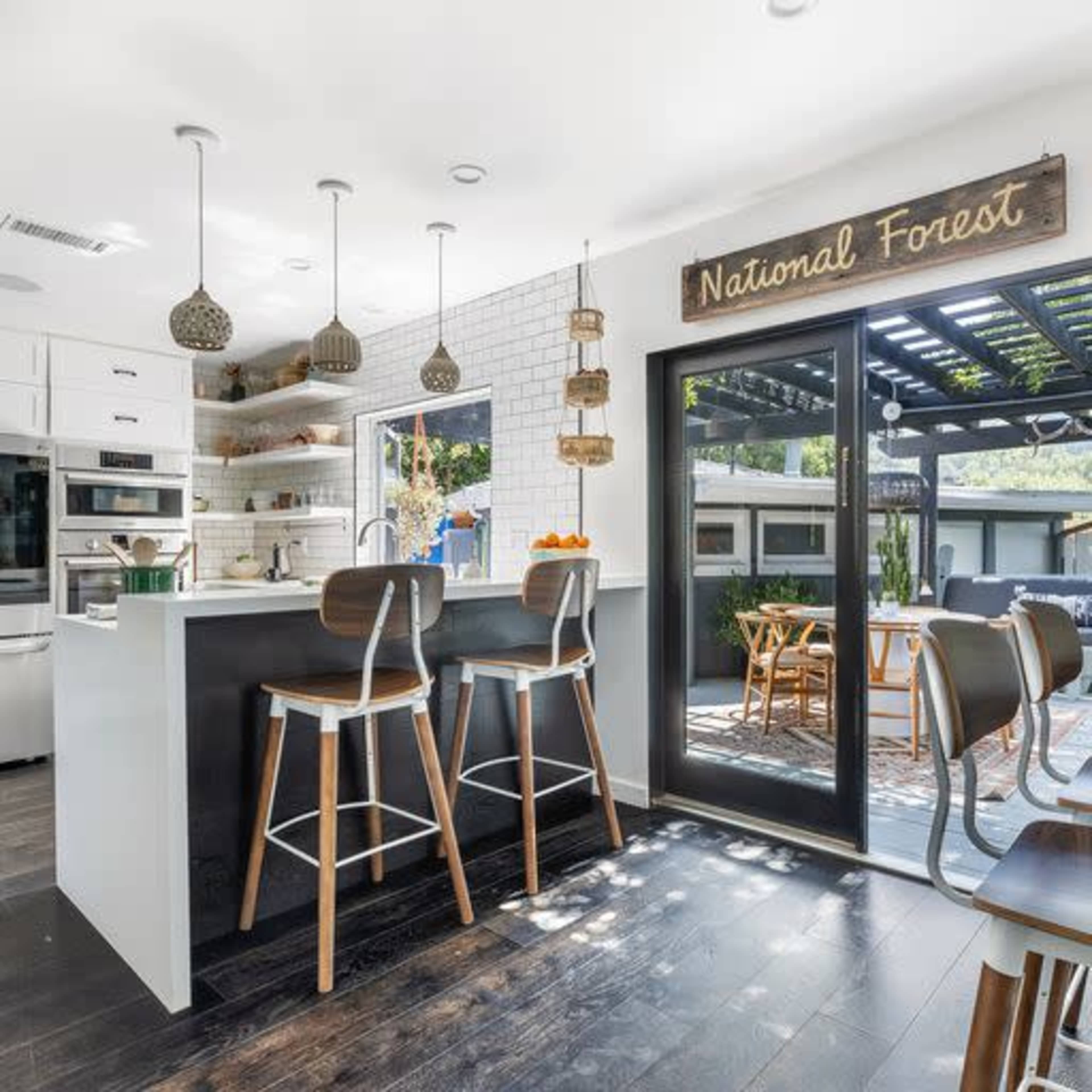 A modern kitchen features white cabinetry, pendant lights, and a view of a patio area through large glass doors.