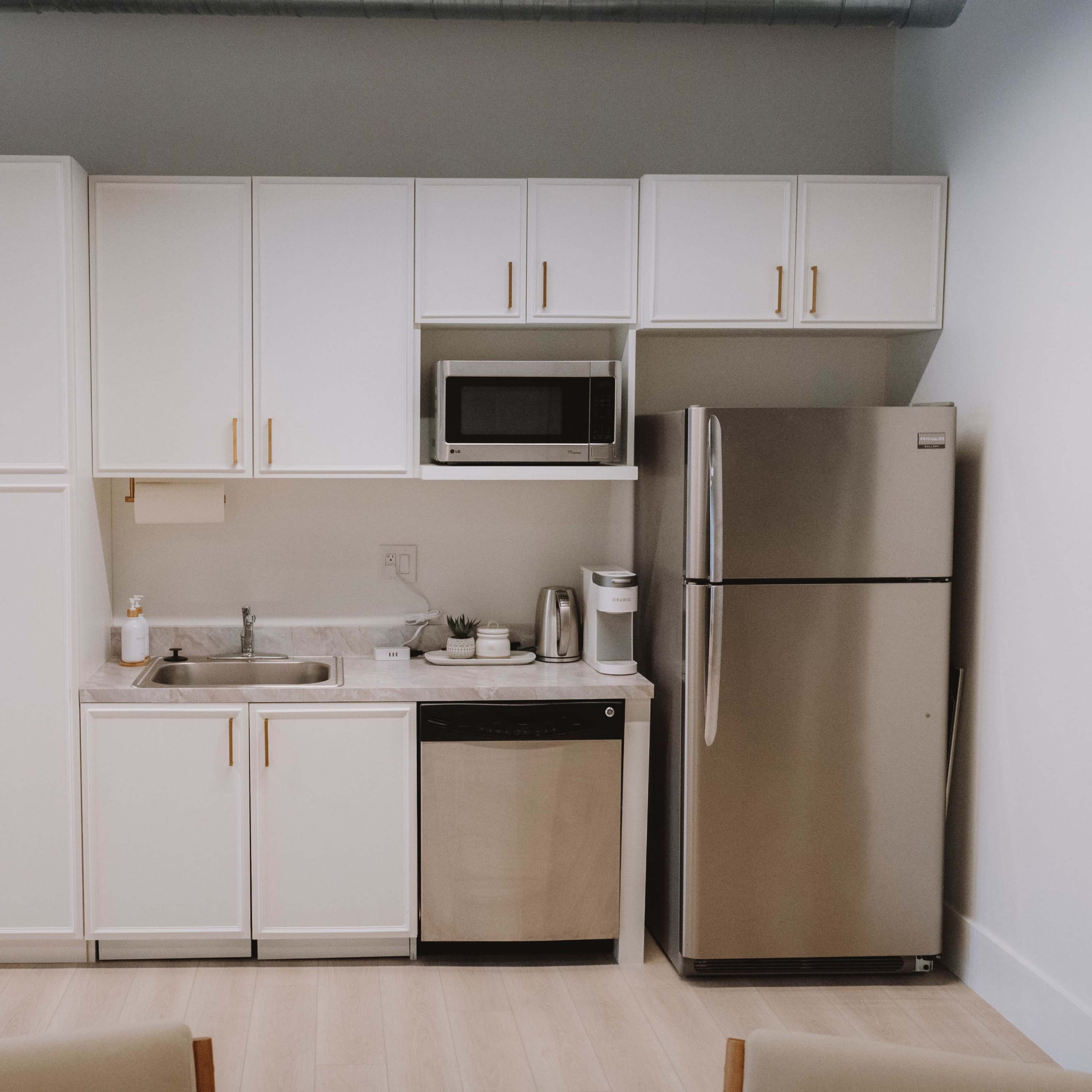 A modern kitchen features white cabinetry, a stainless steel refrigerator, a microwave, a sink, and a dishwasher.