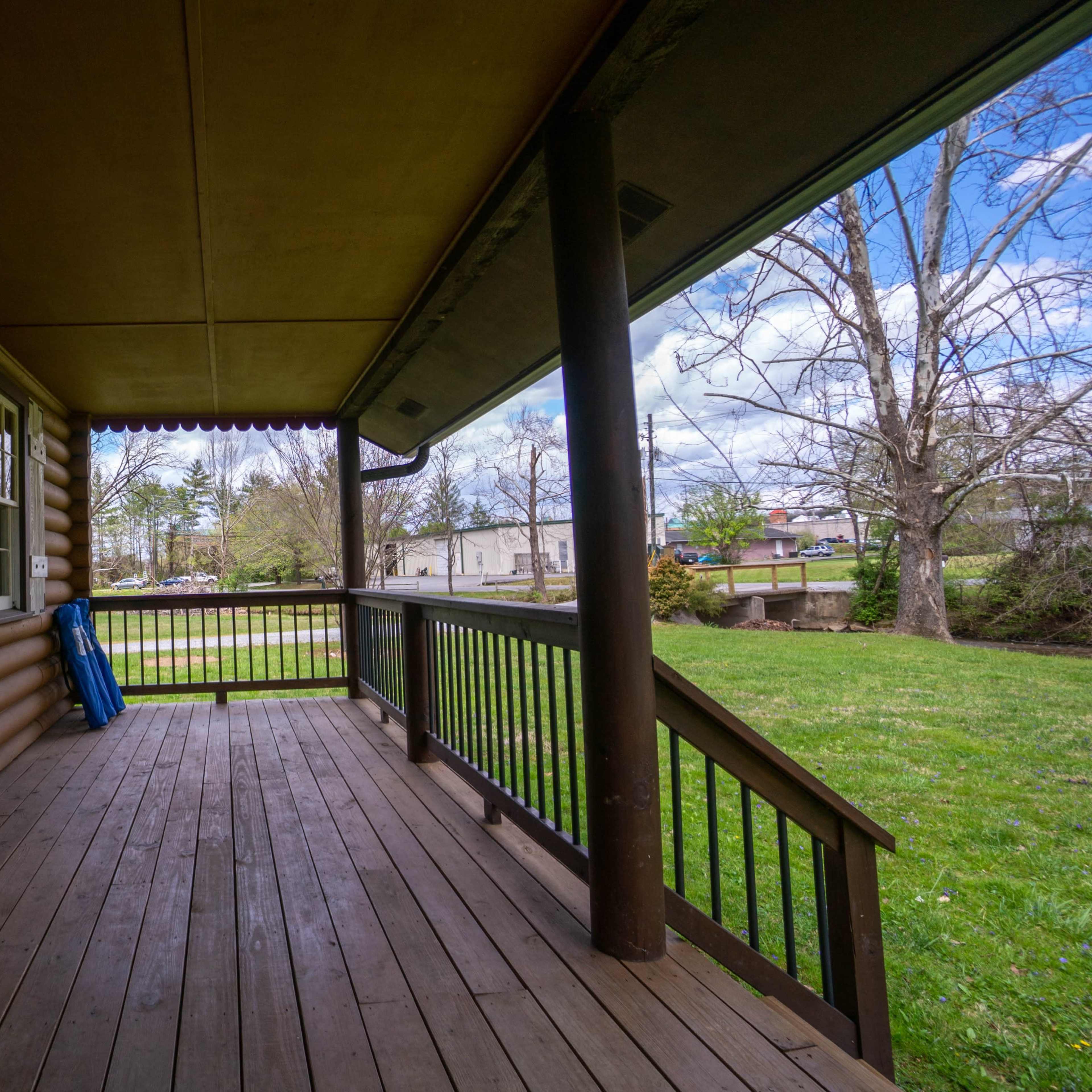 A wooden porch with a view of an expansive grassy area and trees beyond.