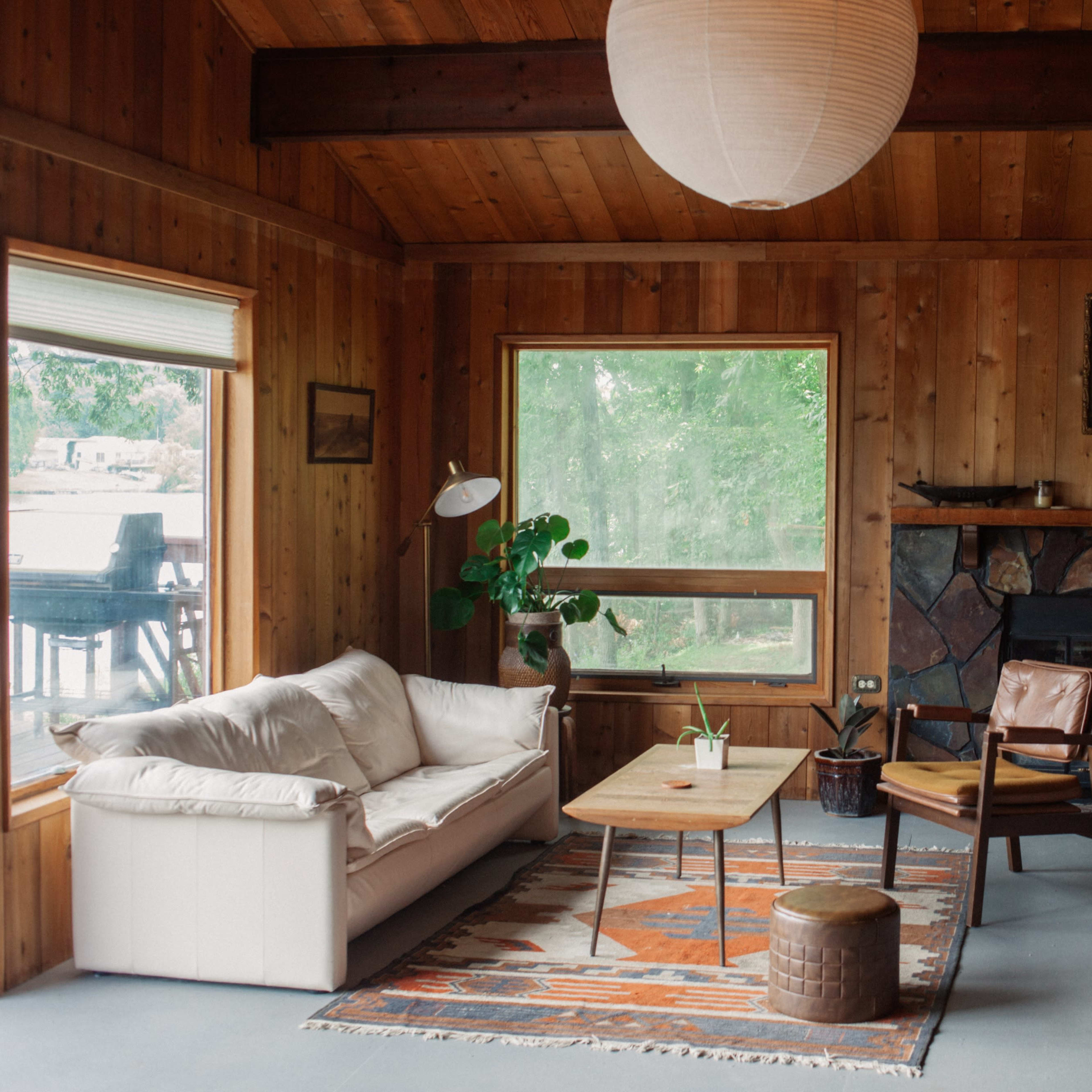 A wooden-paneled living room with a white sofa, a wooden coffee table, and a large window overlooking greenery.