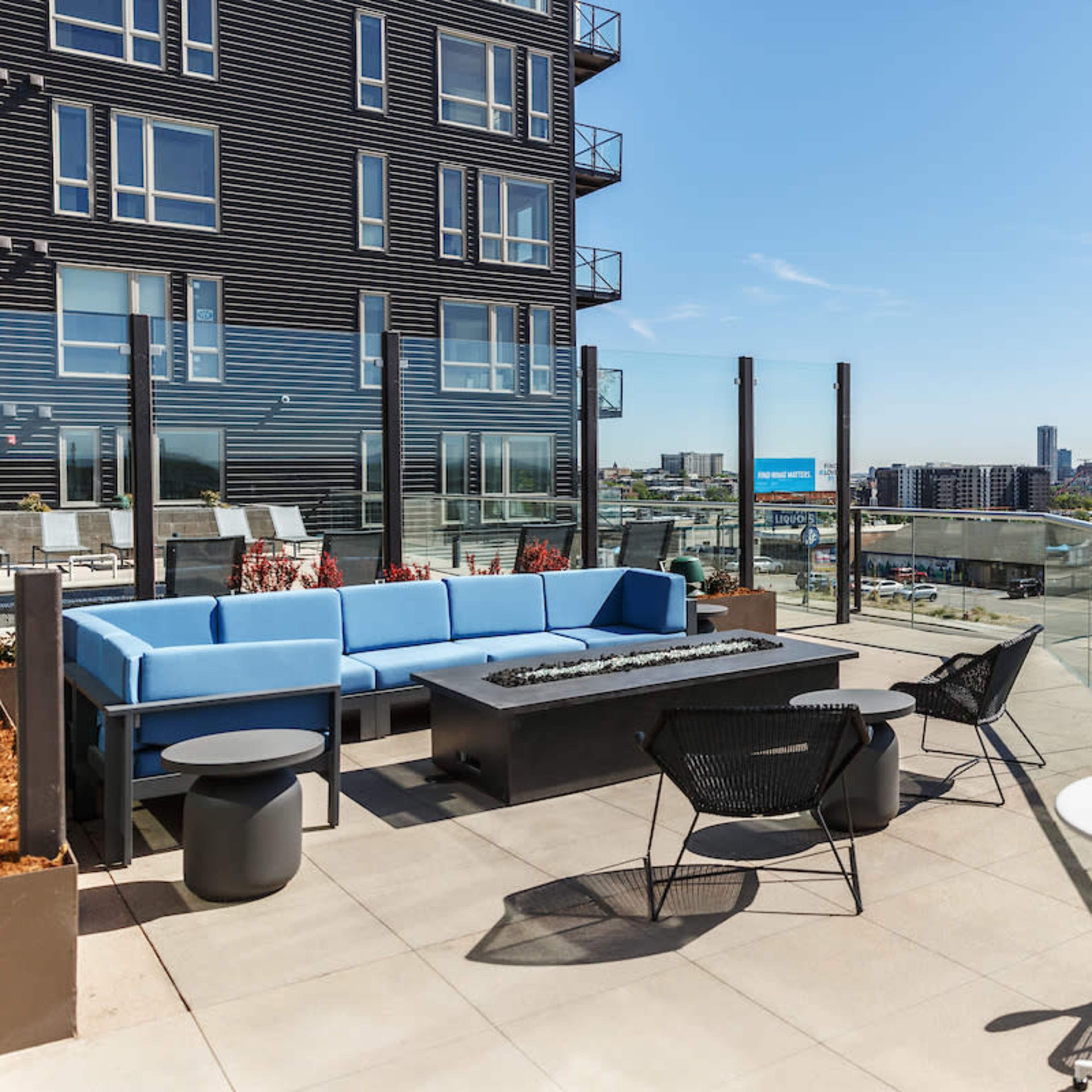 A rooftop terrace with modern furniture, overlooking a stadium and city skyline.