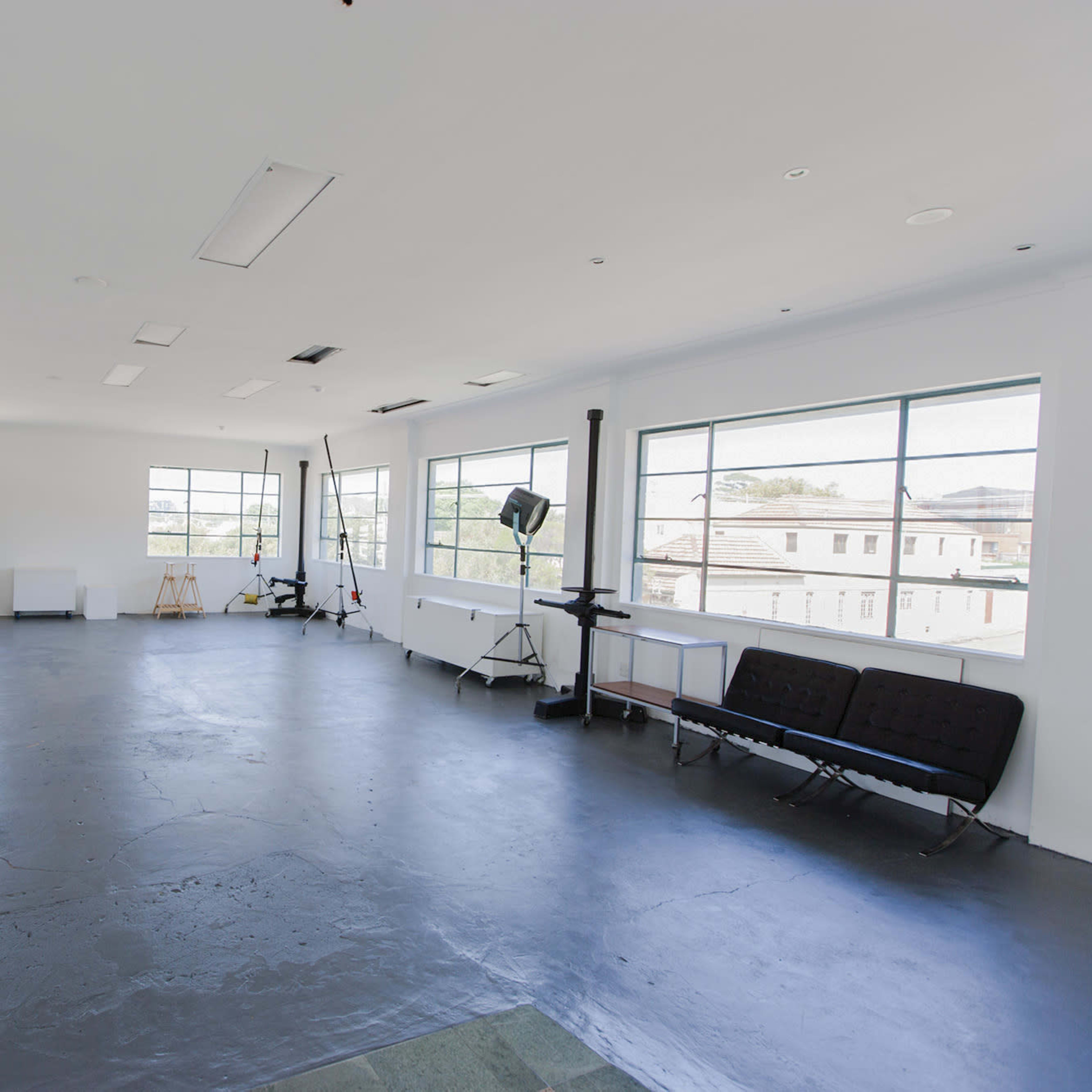 A spacious, empty studio with large windows, minimal furniture, and a polished concrete floor.