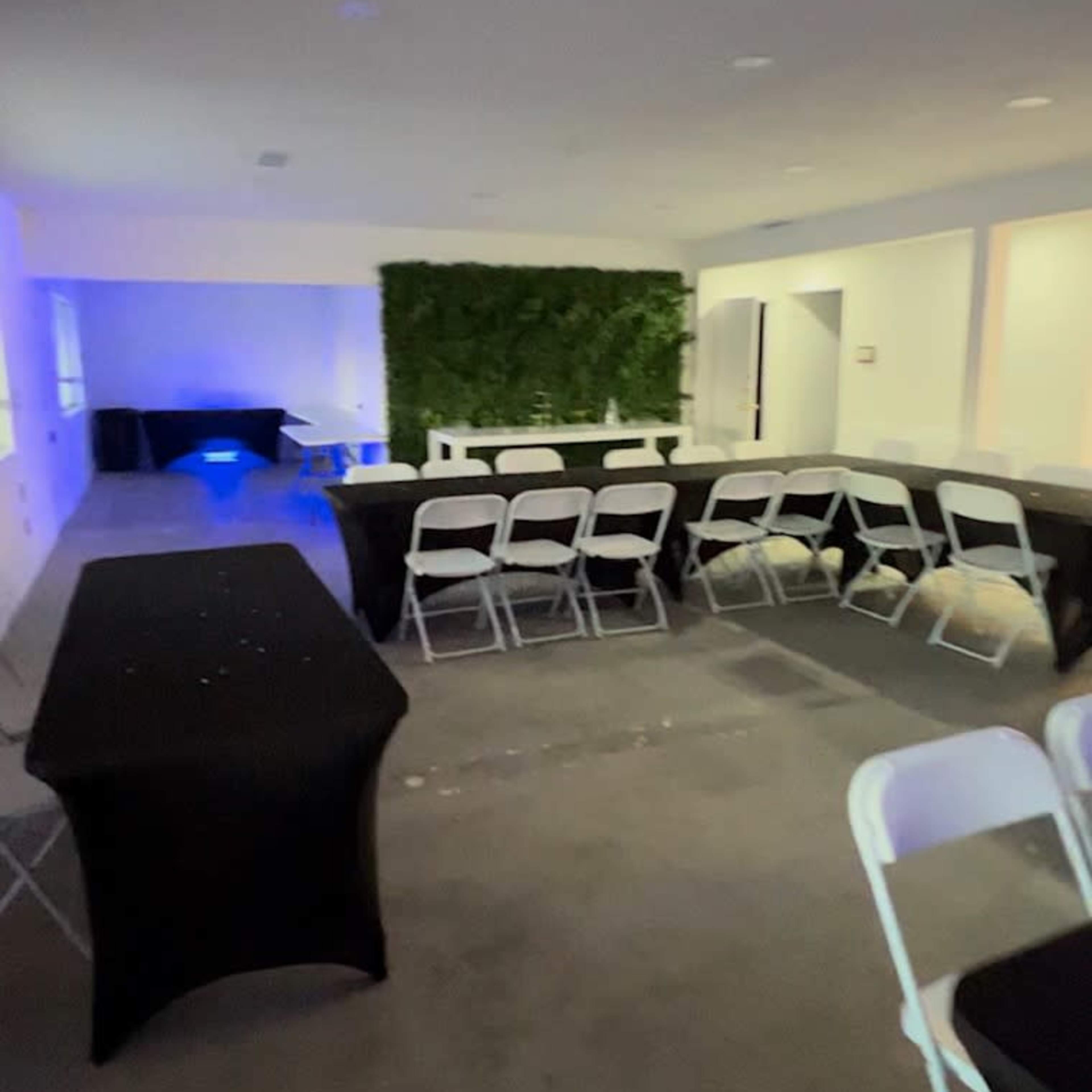 An empty event space with black and white chairs arranged around several tables, and a green wall in the background.