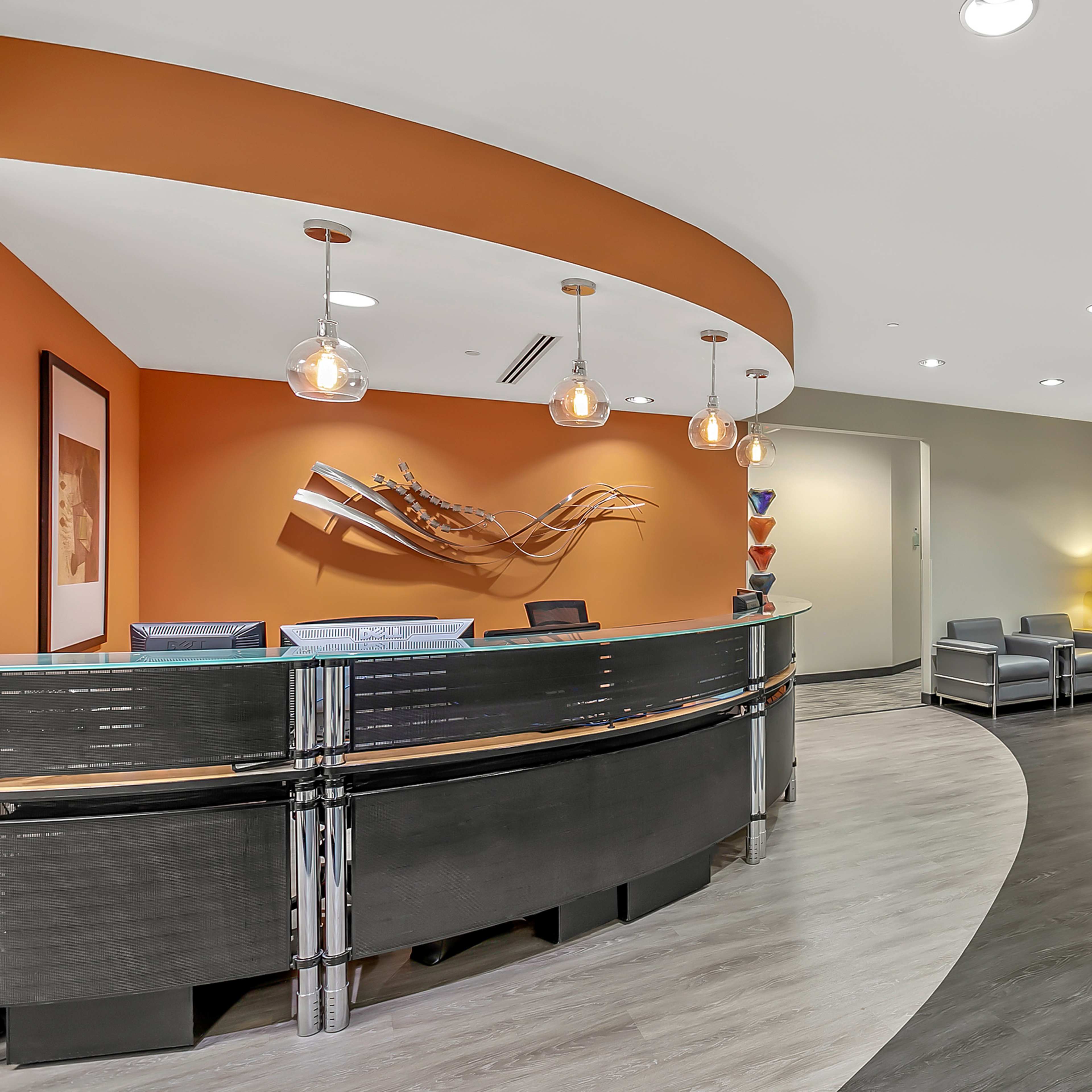 A modern reception area with a curved front desk, orange accent wall, and seating arrangements.