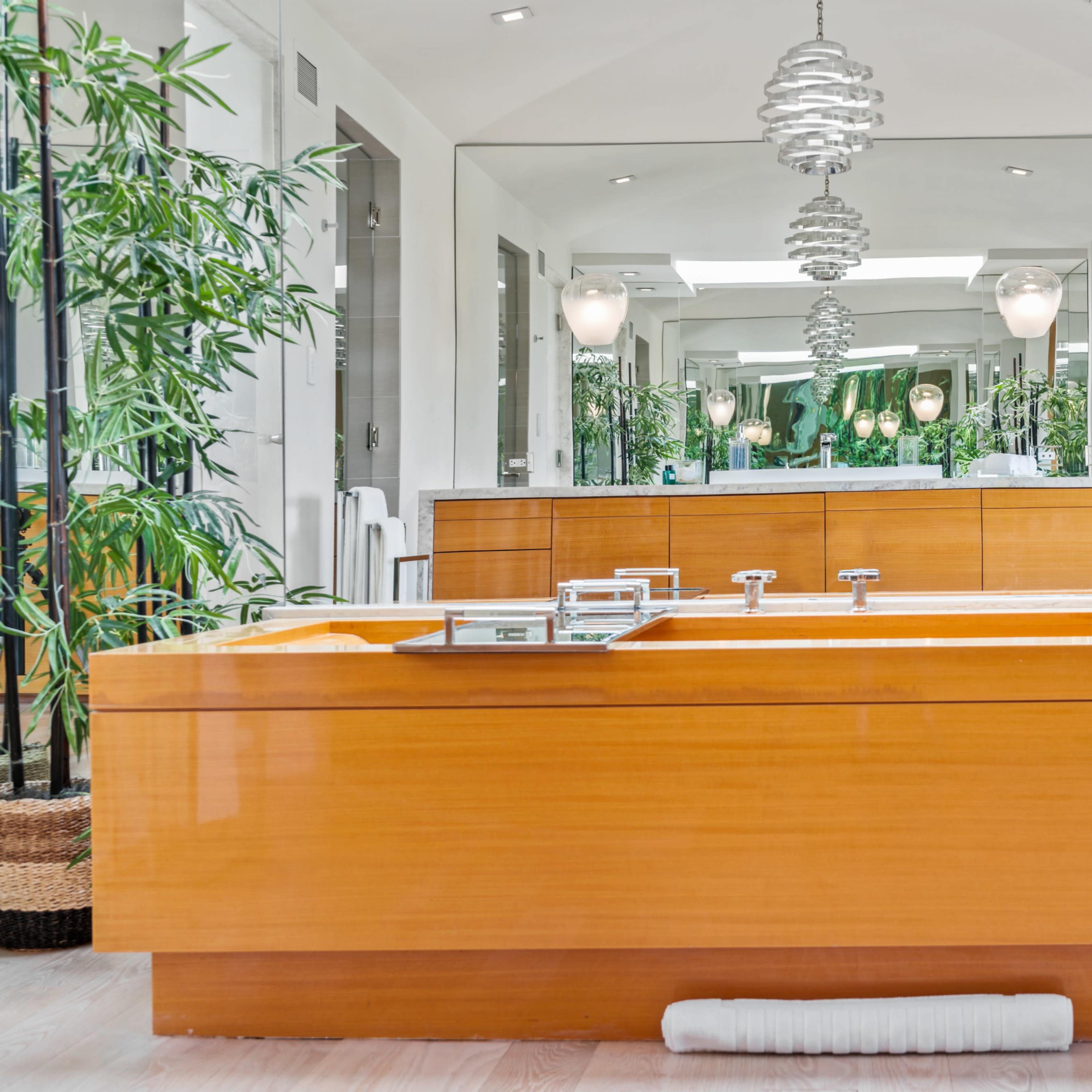 A modern bathroom features a wooden bathtub surrounded by bamboo plants and contemporary lighting fixtures.