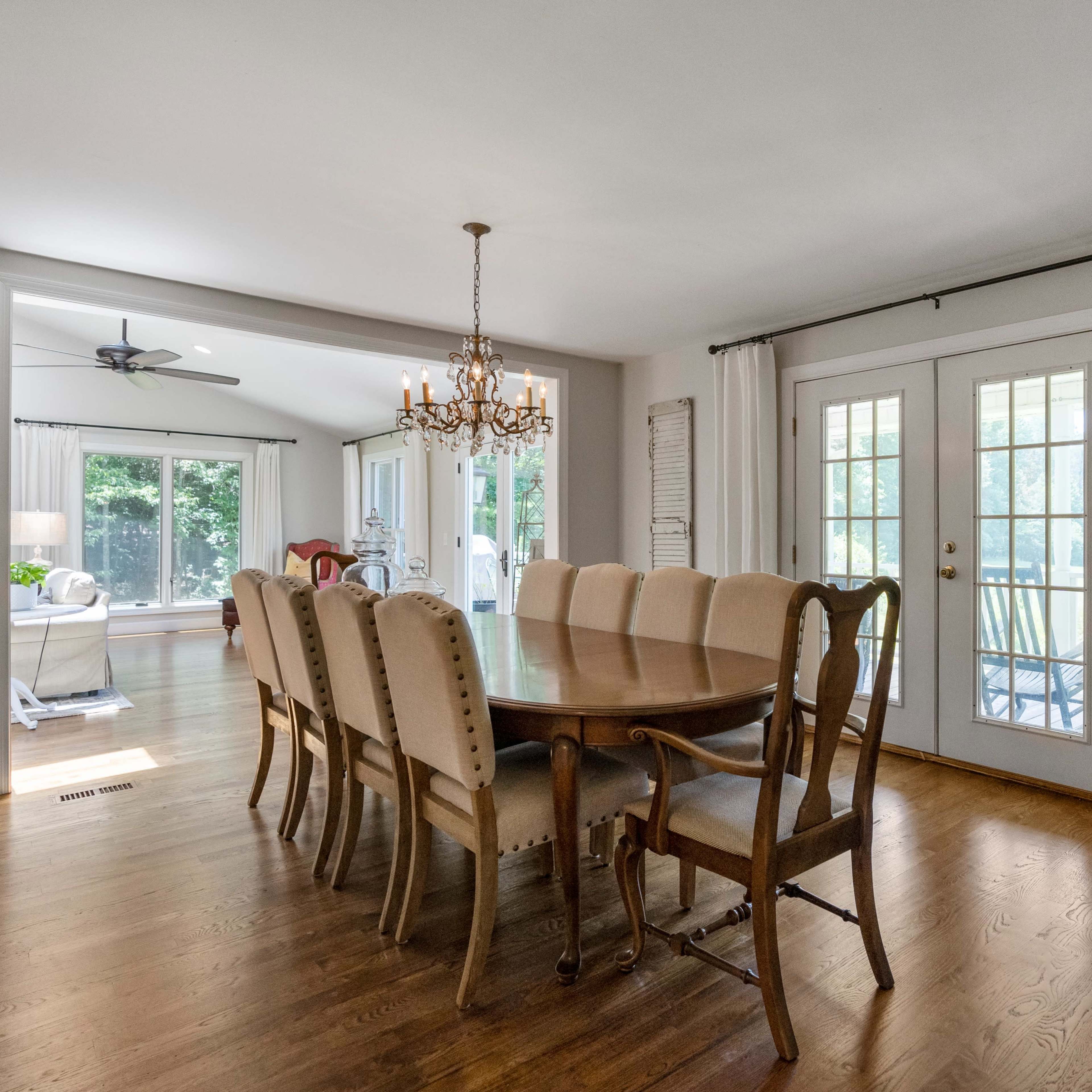 A spacious dining room features a large wooden table surrounded by upholstered chairs, leading to a set of glass doors that open to an outdoor area.