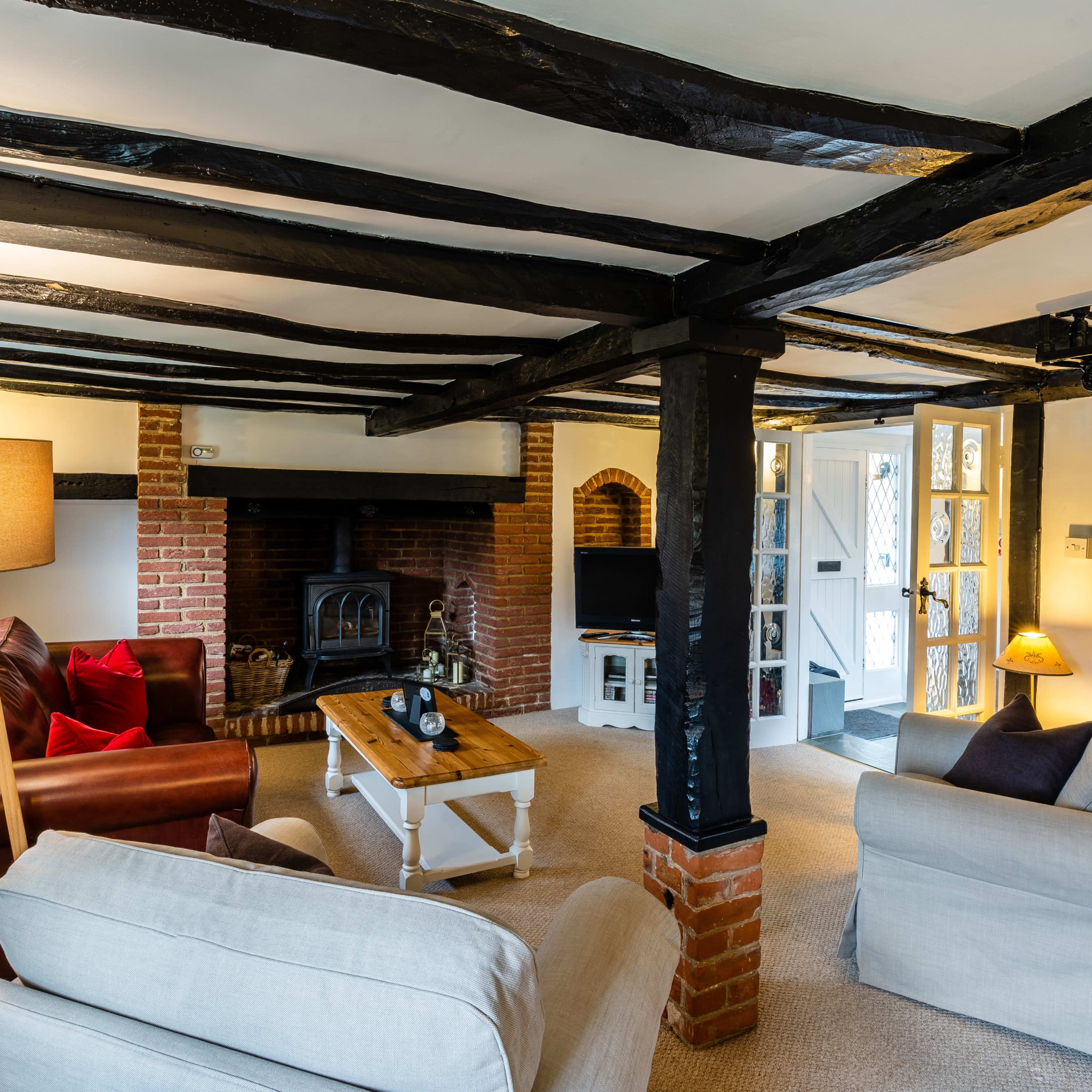 A cozy living room features exposed wooden beams, a brick fireplace, and comfortable seating arranged around a central coffee table.