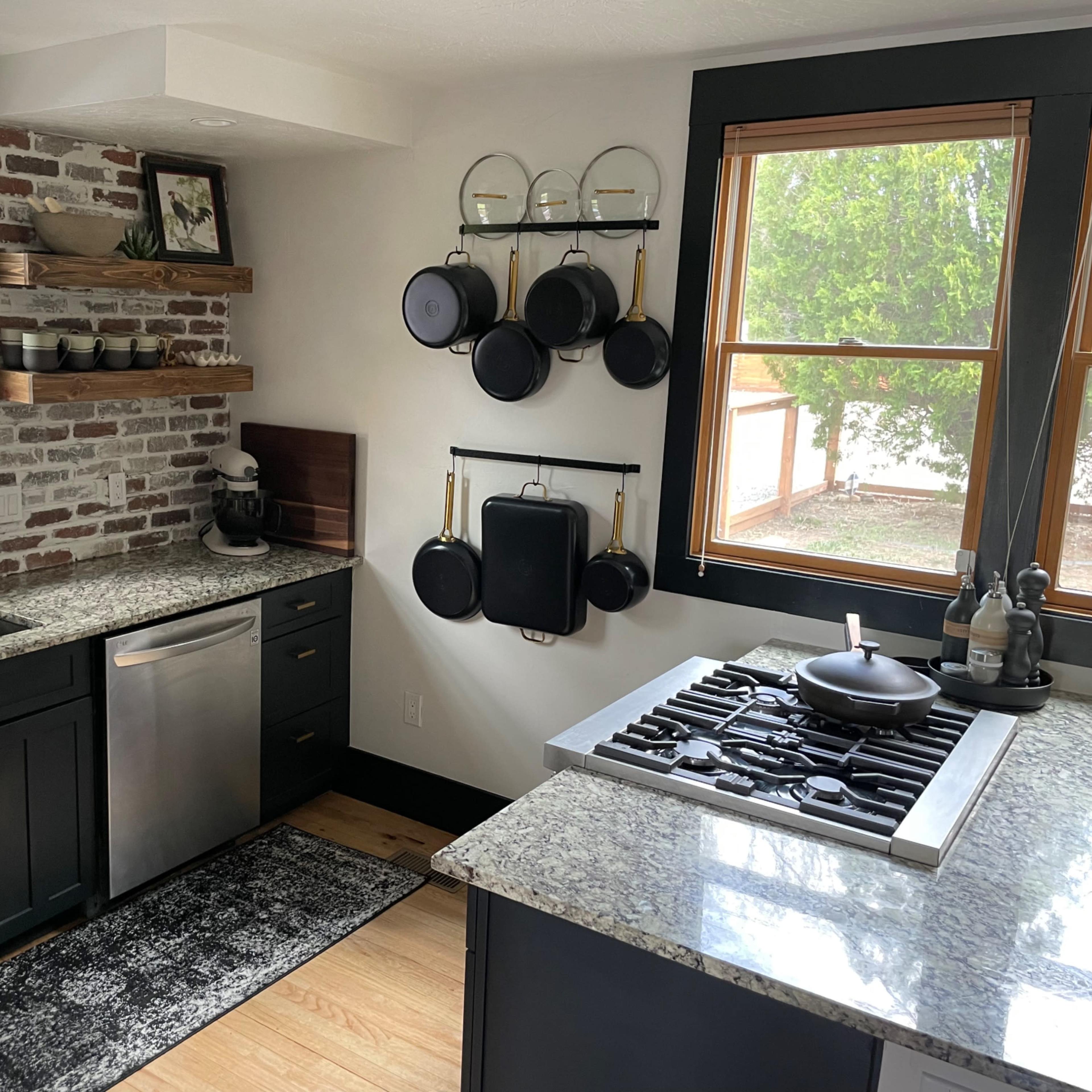 A modern kitchen featuring dark cabinetry, granite countertops, a gas stove, and an exposed brick wall.