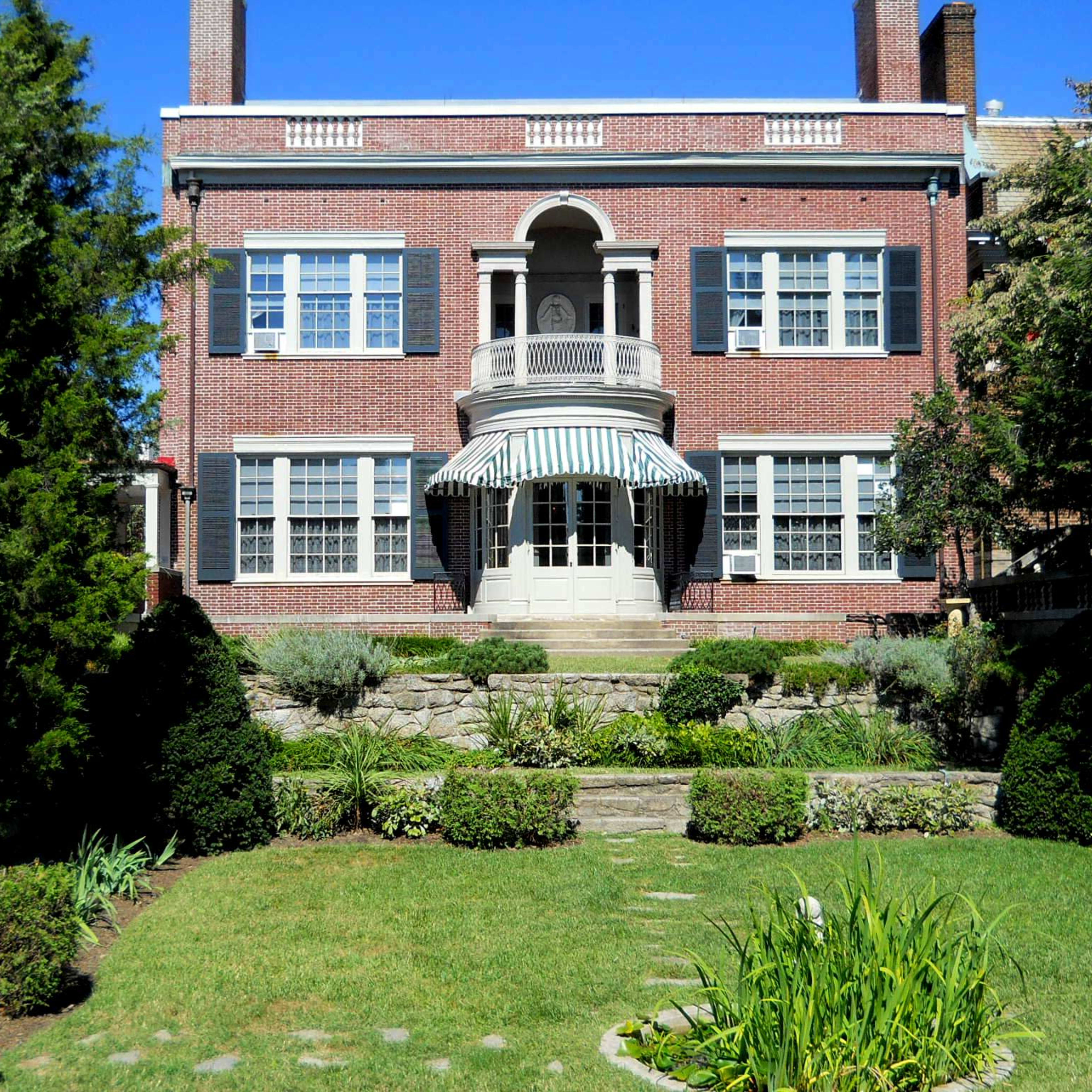 A brick house with a covered porch, surrounded by landscaped gardens and pathways.