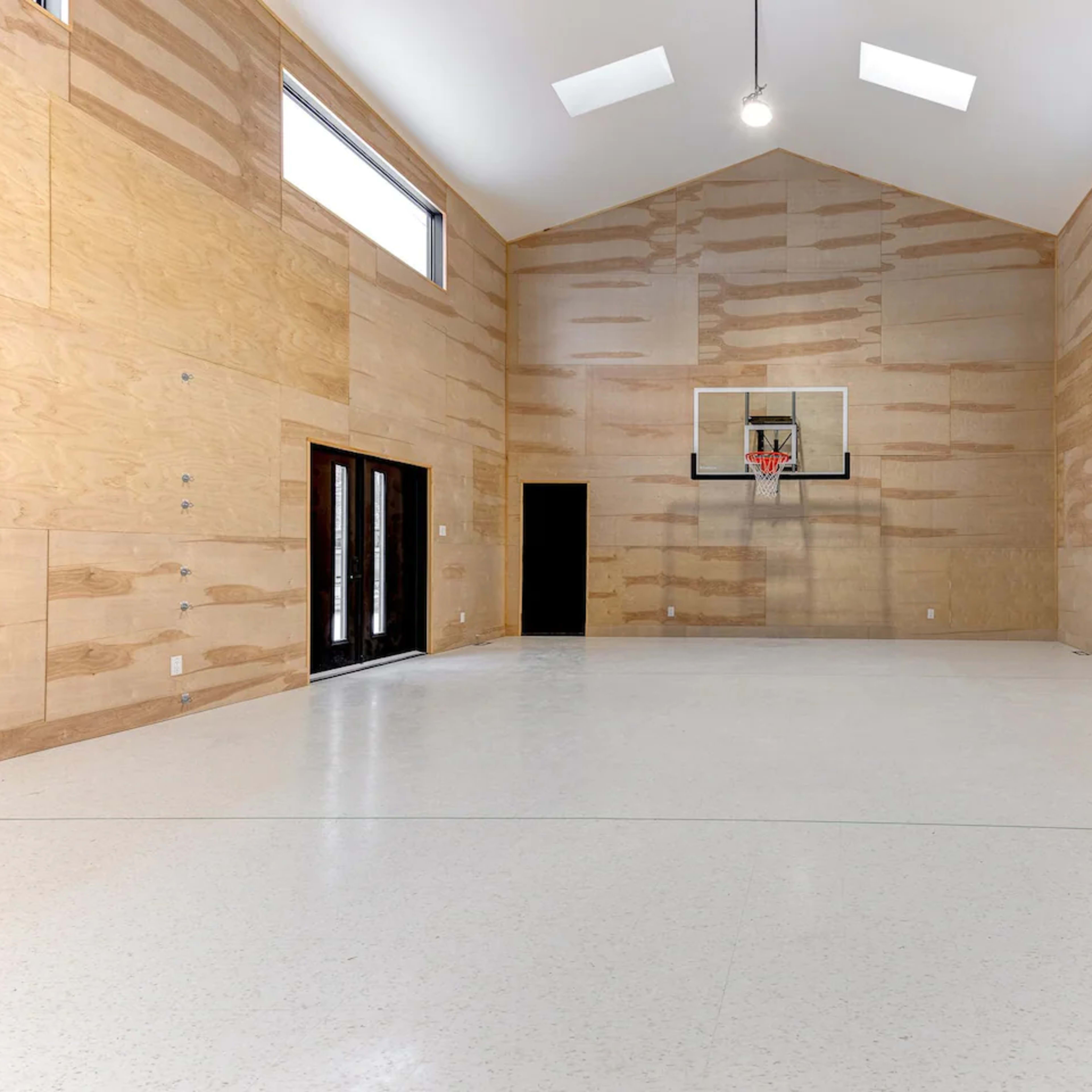 An indoor basketball court with wooden walls and a basketball hoop mounted at one end.
