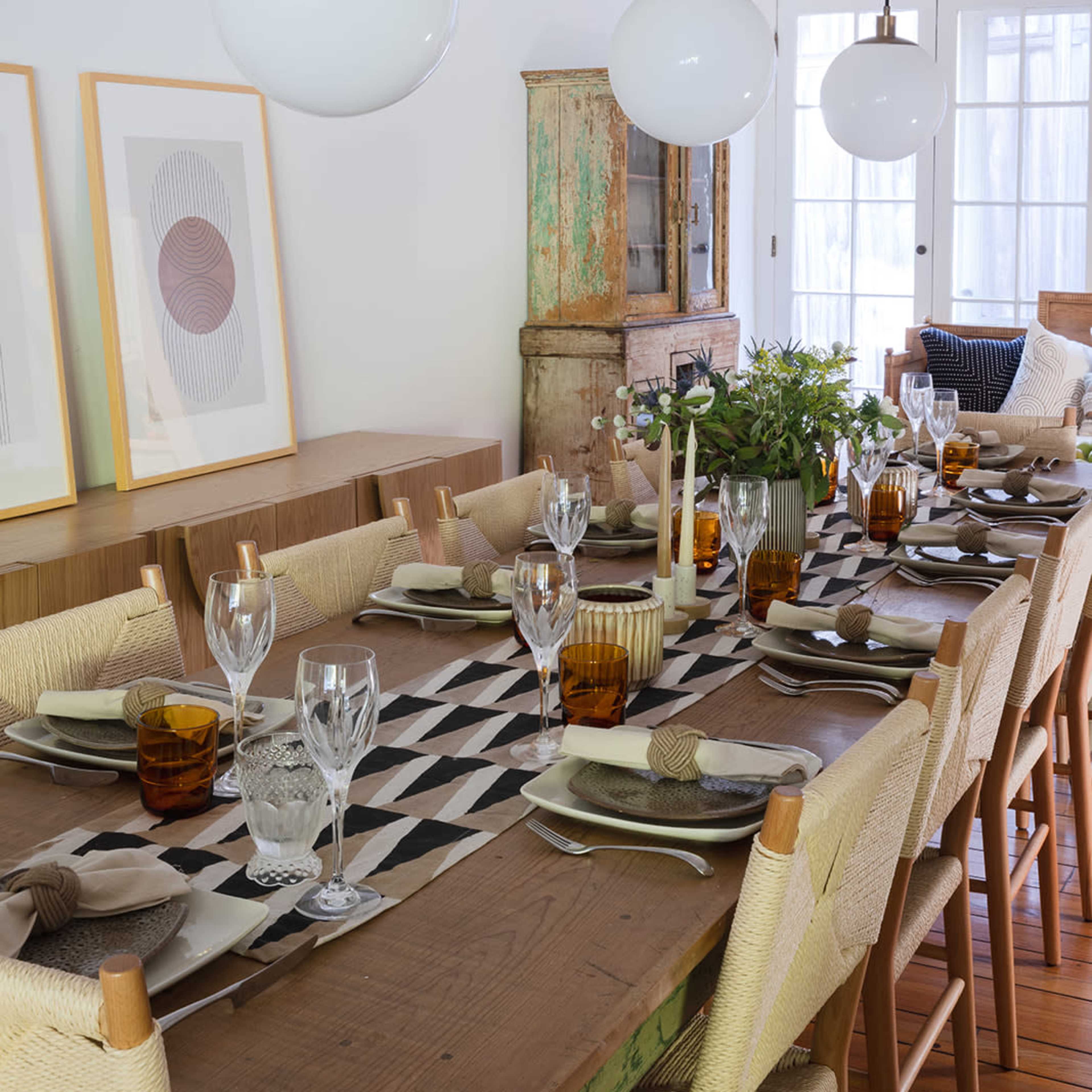 A dining room features a long wooden table set with glasses and plates, illuminated by three globe pendant lights above.