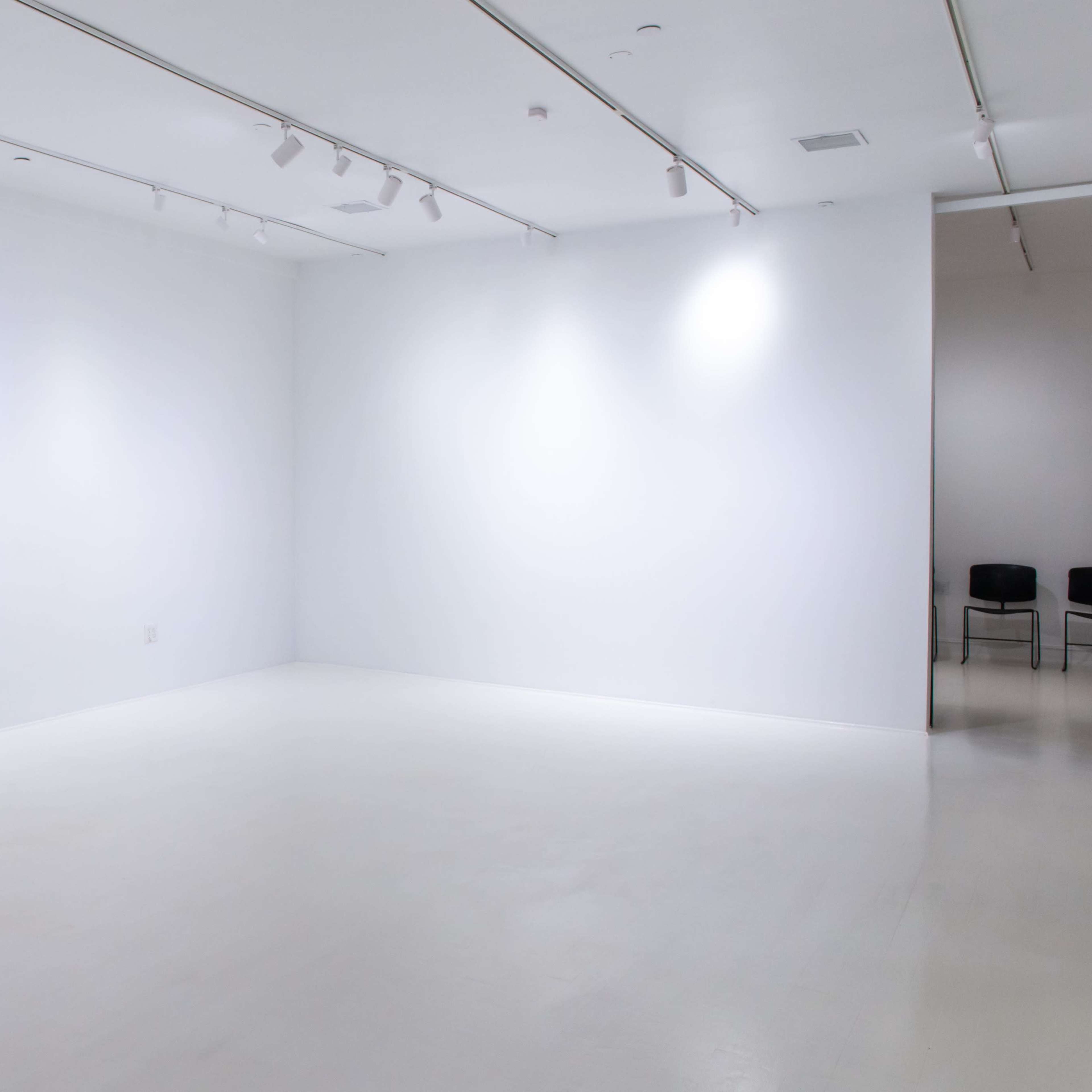 A large, empty, well-lit gallery space with white walls and a polished floor.