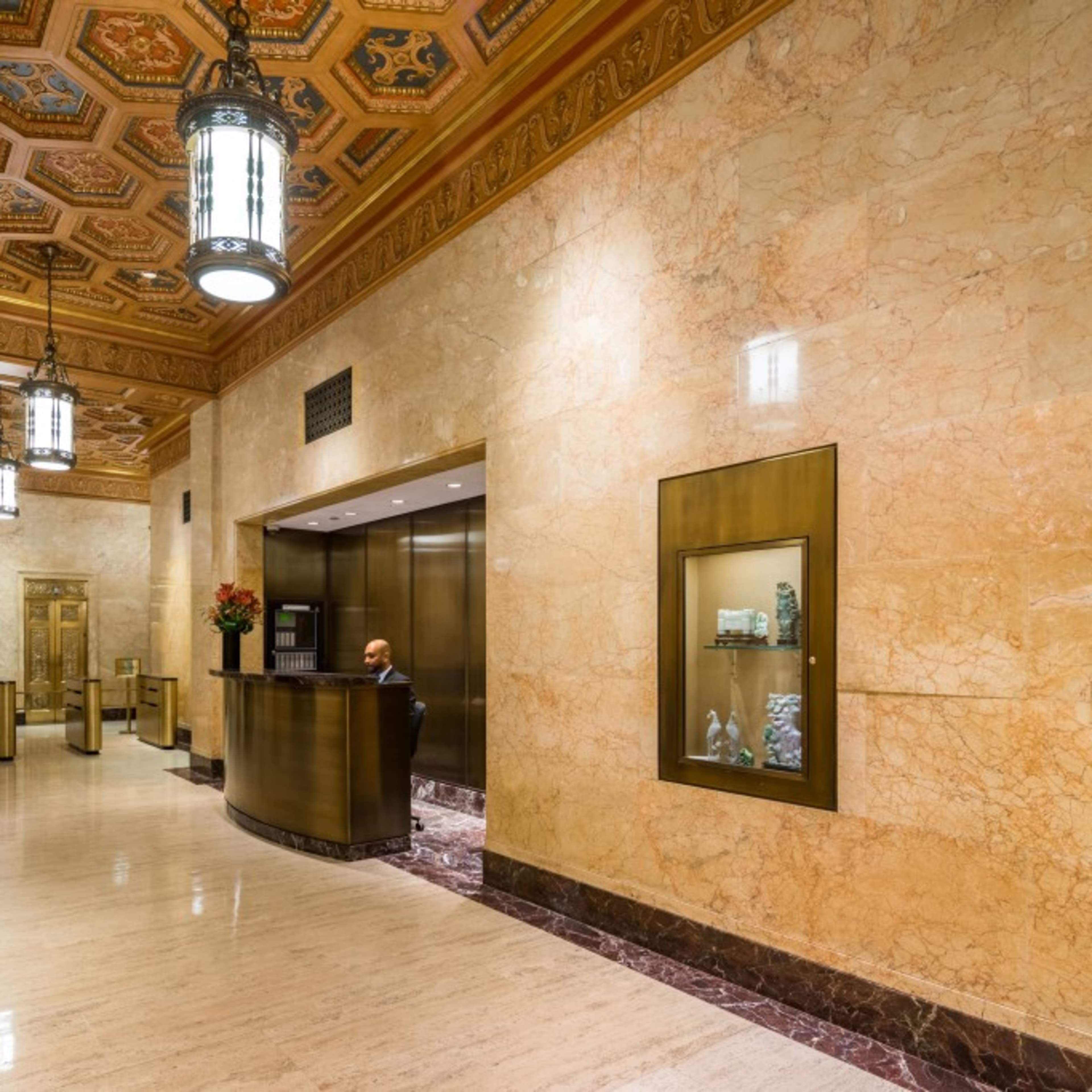 A marble-finished lobby with ornate lighting fixtures and an elevator area, featuring a receptionist at a front desk.