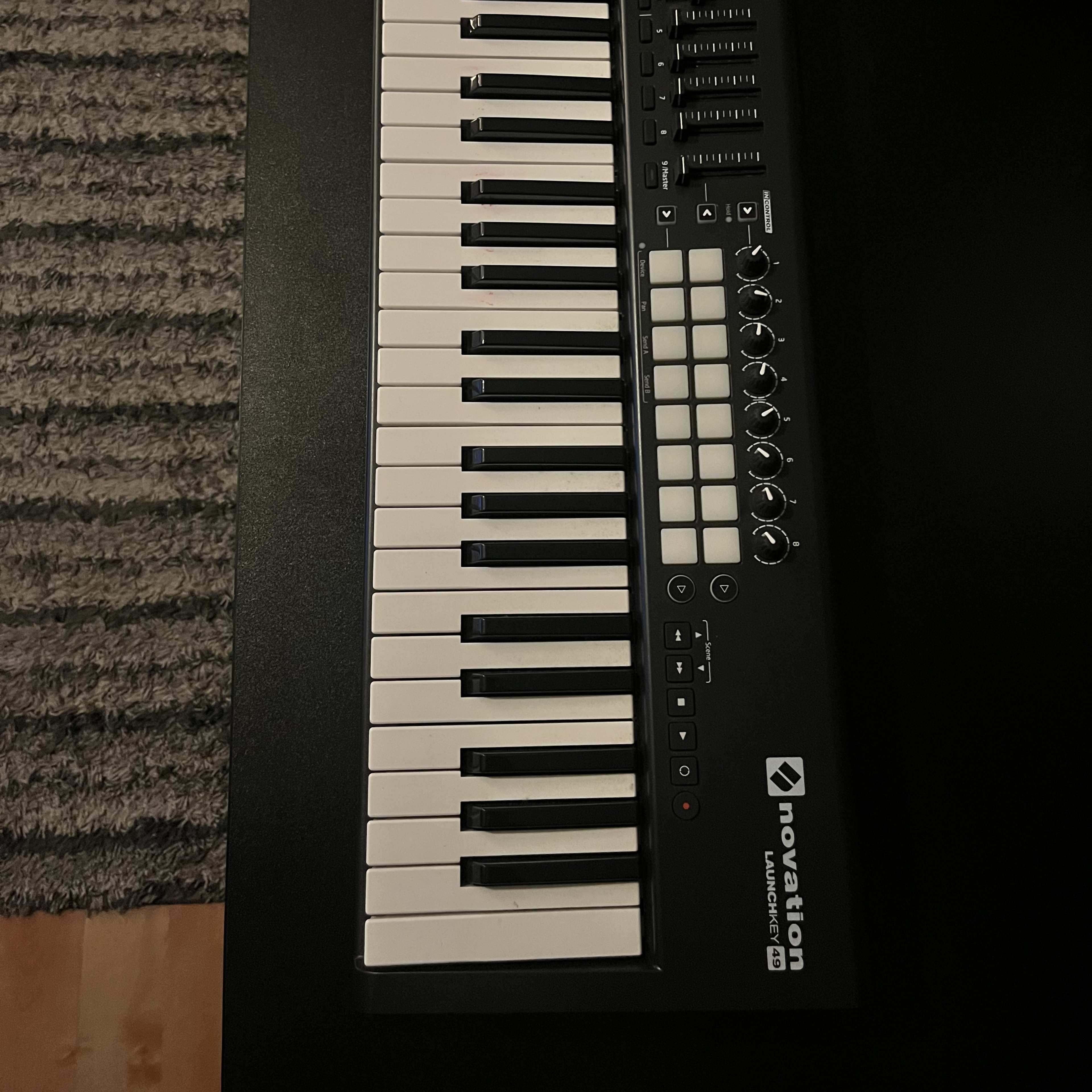 A Novation Launchkey MIDI keyboard with black keys, white keys, and various control knobs and pads, resting on a dark surface.
