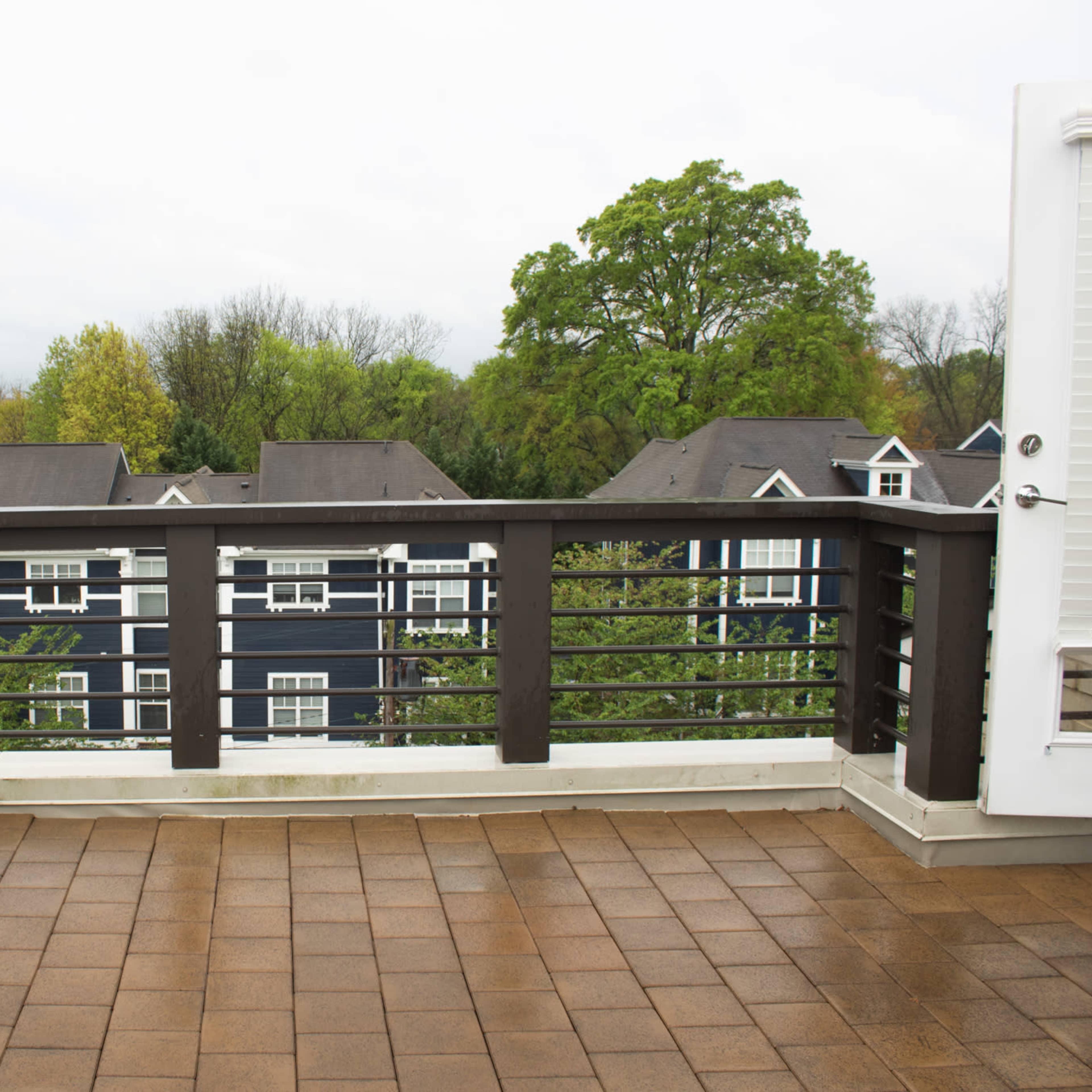 A spacious, empty balcony with a railing overlooking a neighborhood of multi-story buildings under cloudy skies.